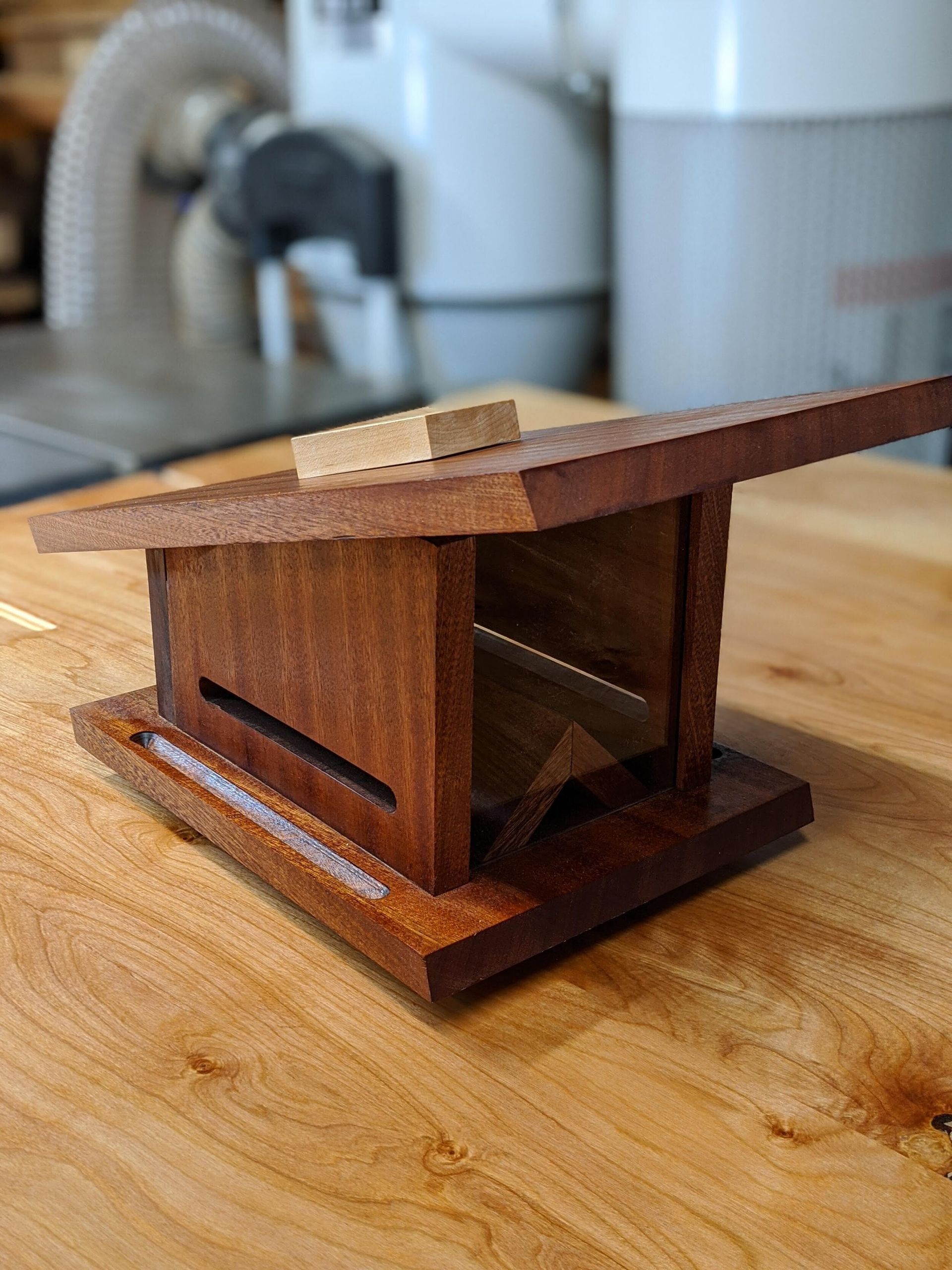 A small wooden bird feeder is sitting on a wooden table.