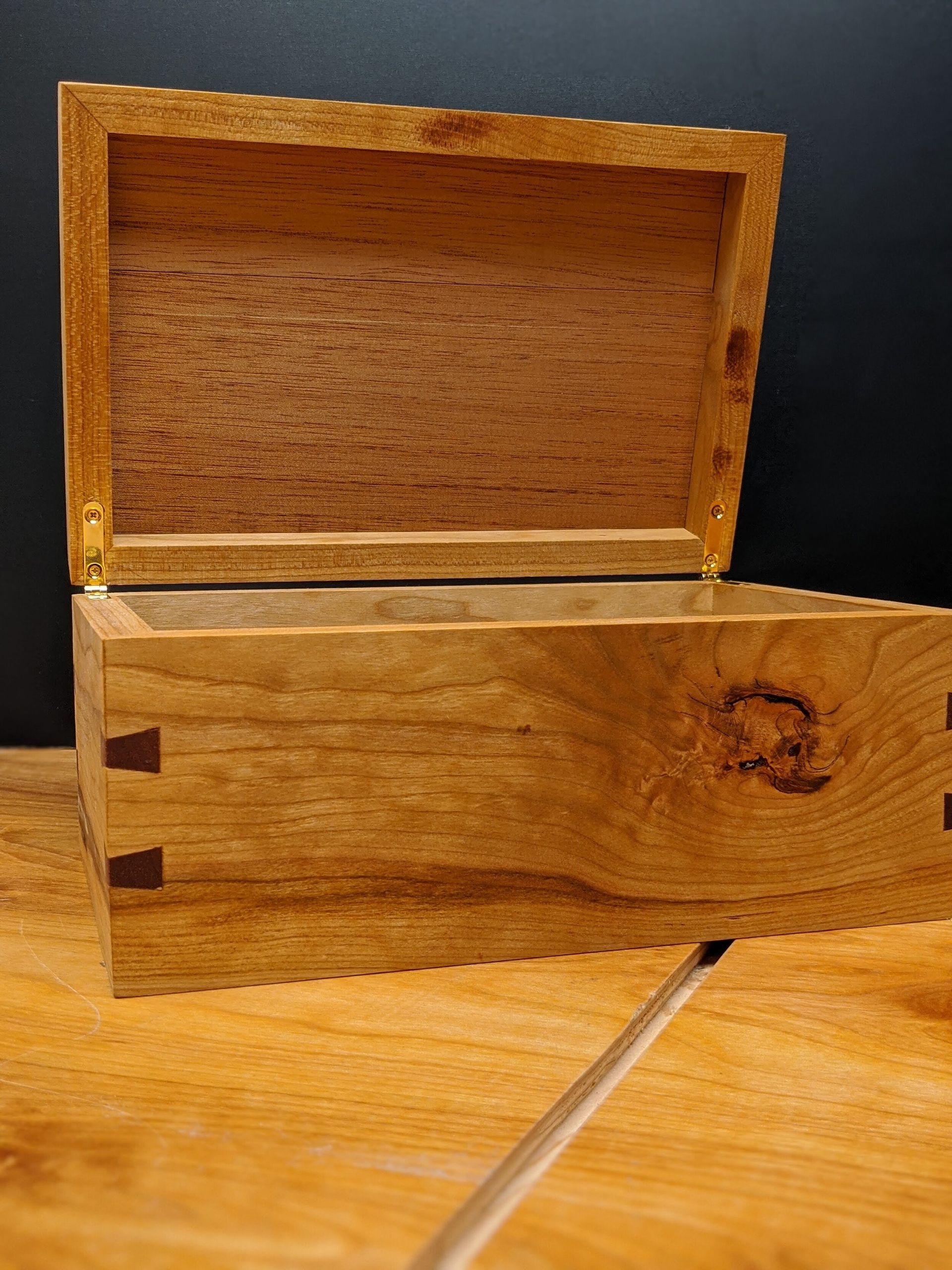 A wooden box with the lid open is sitting on a wooden table.