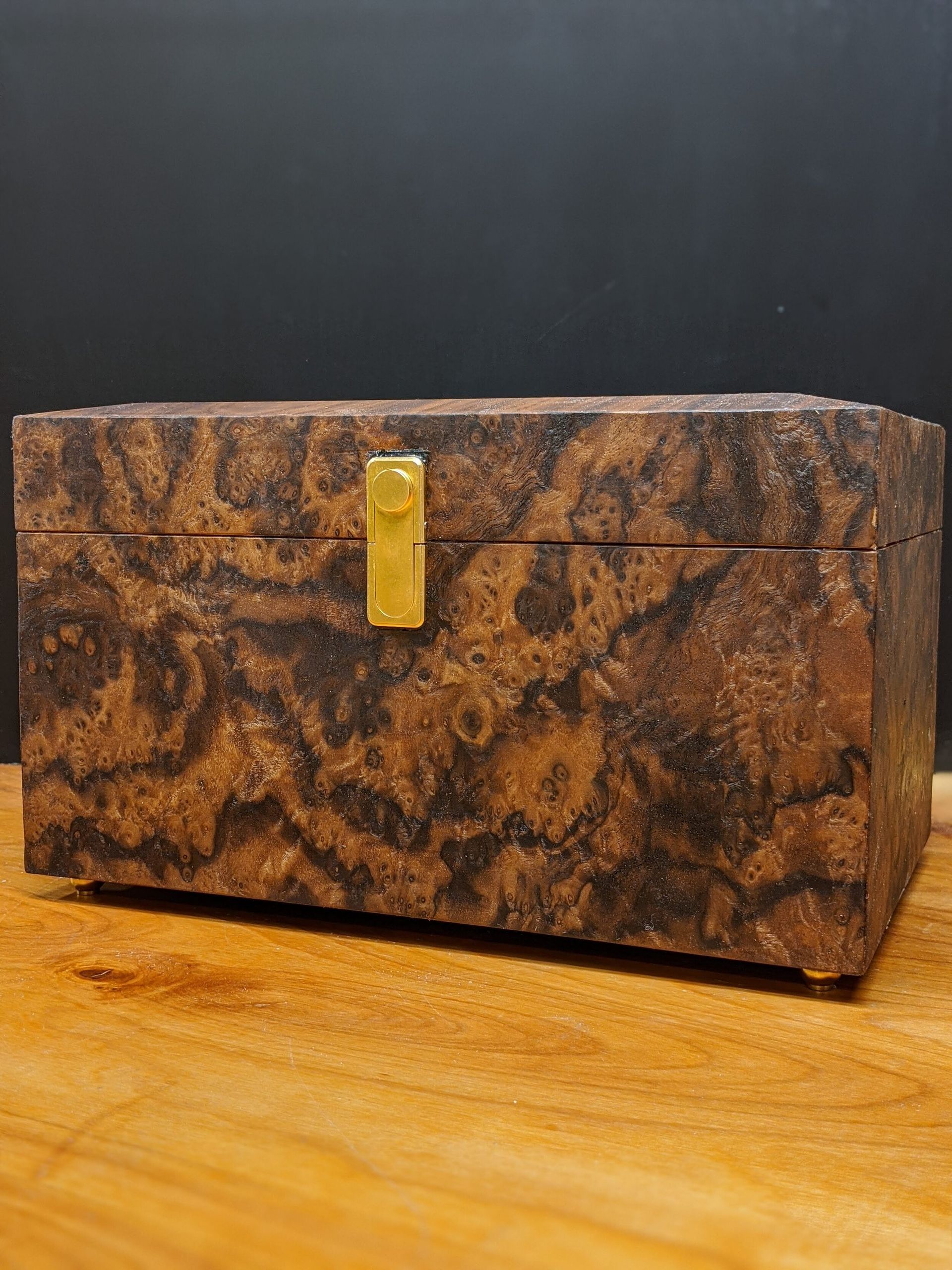 A wooden box with a gold lock is sitting on a wooden table.