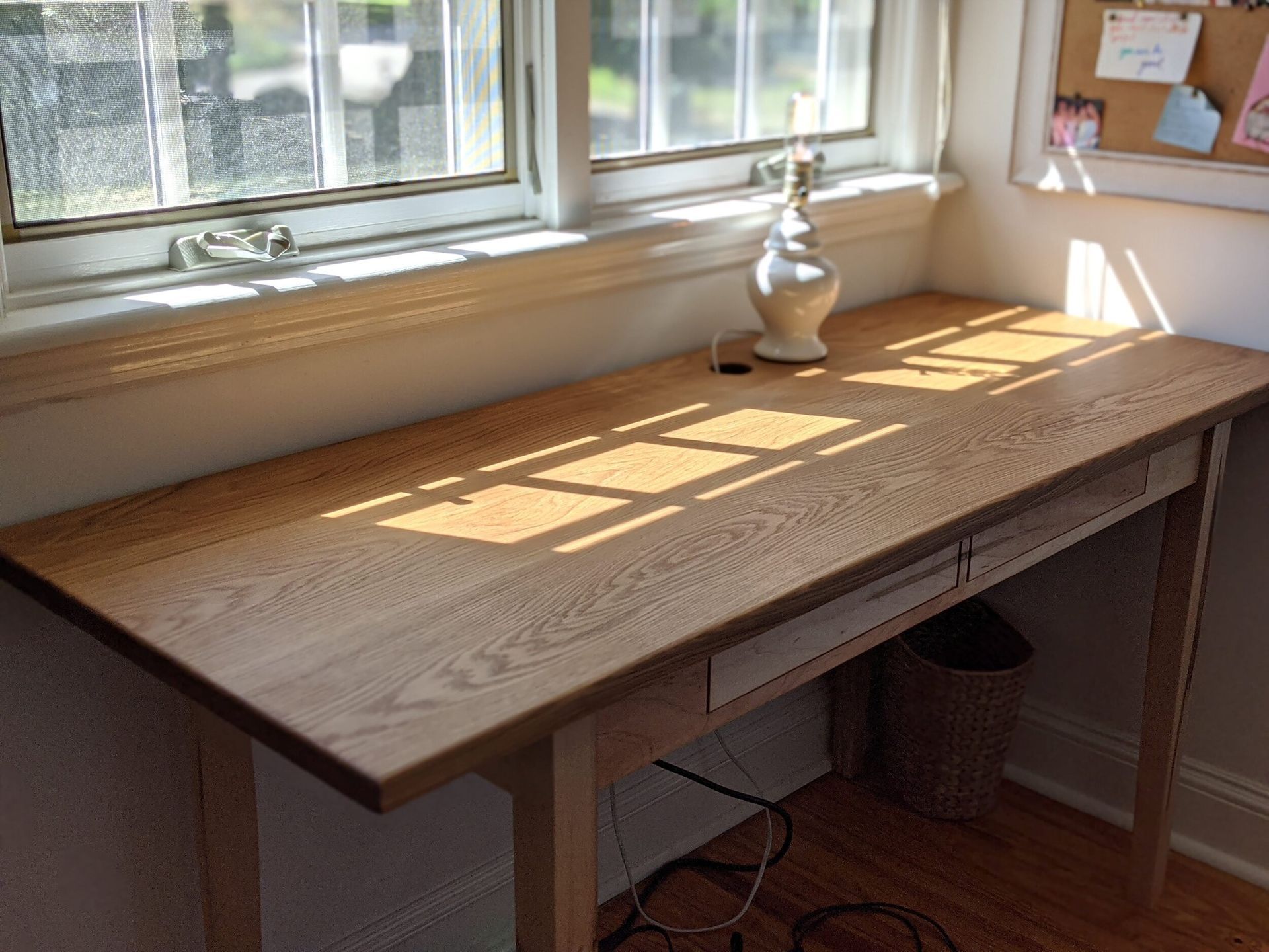 A wooden desk in front of a window with a lamp on it