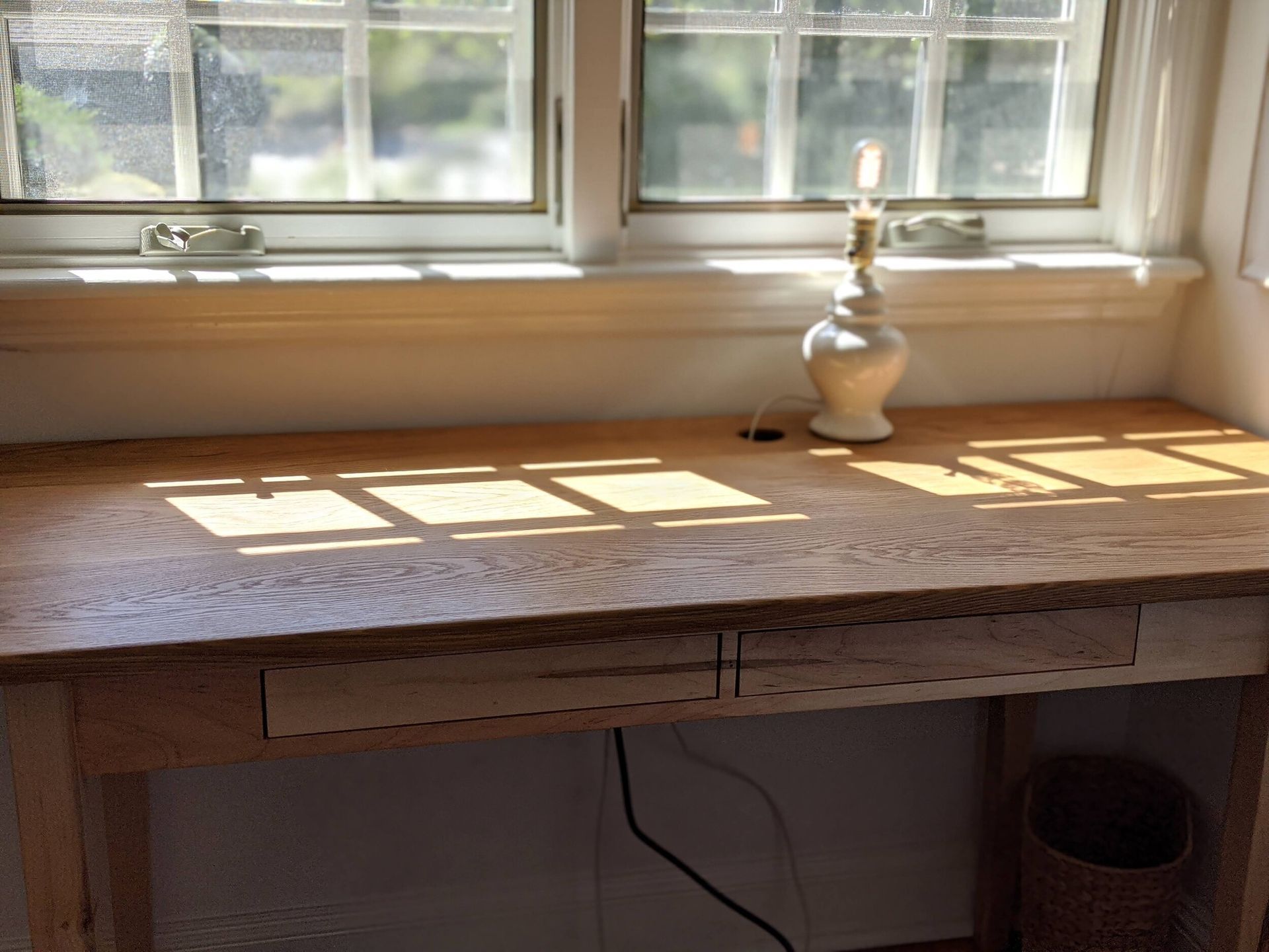 A wooden desk with a lamp on it in front of a window