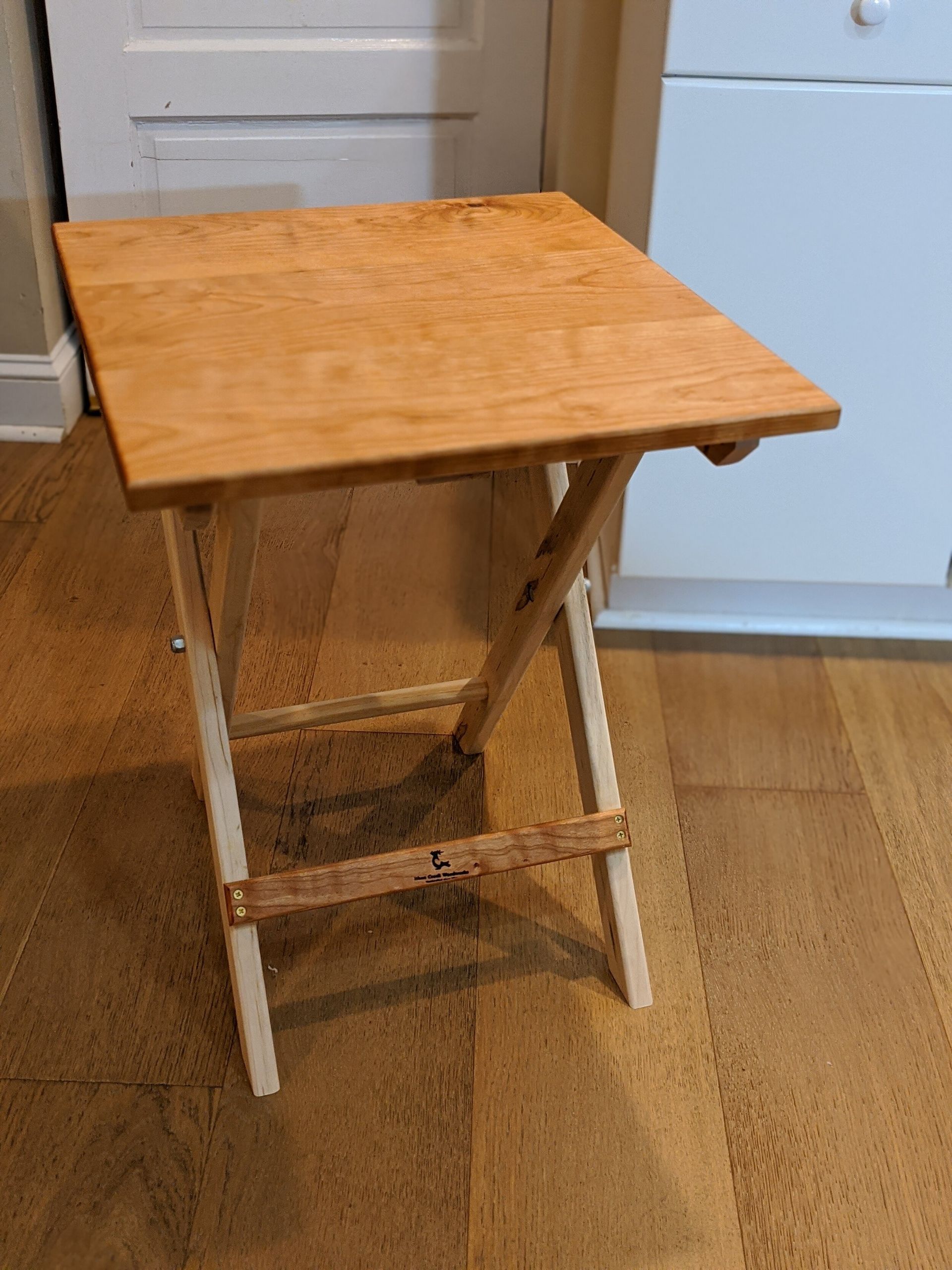 A small wooden folding table is sitting on a wooden floor.