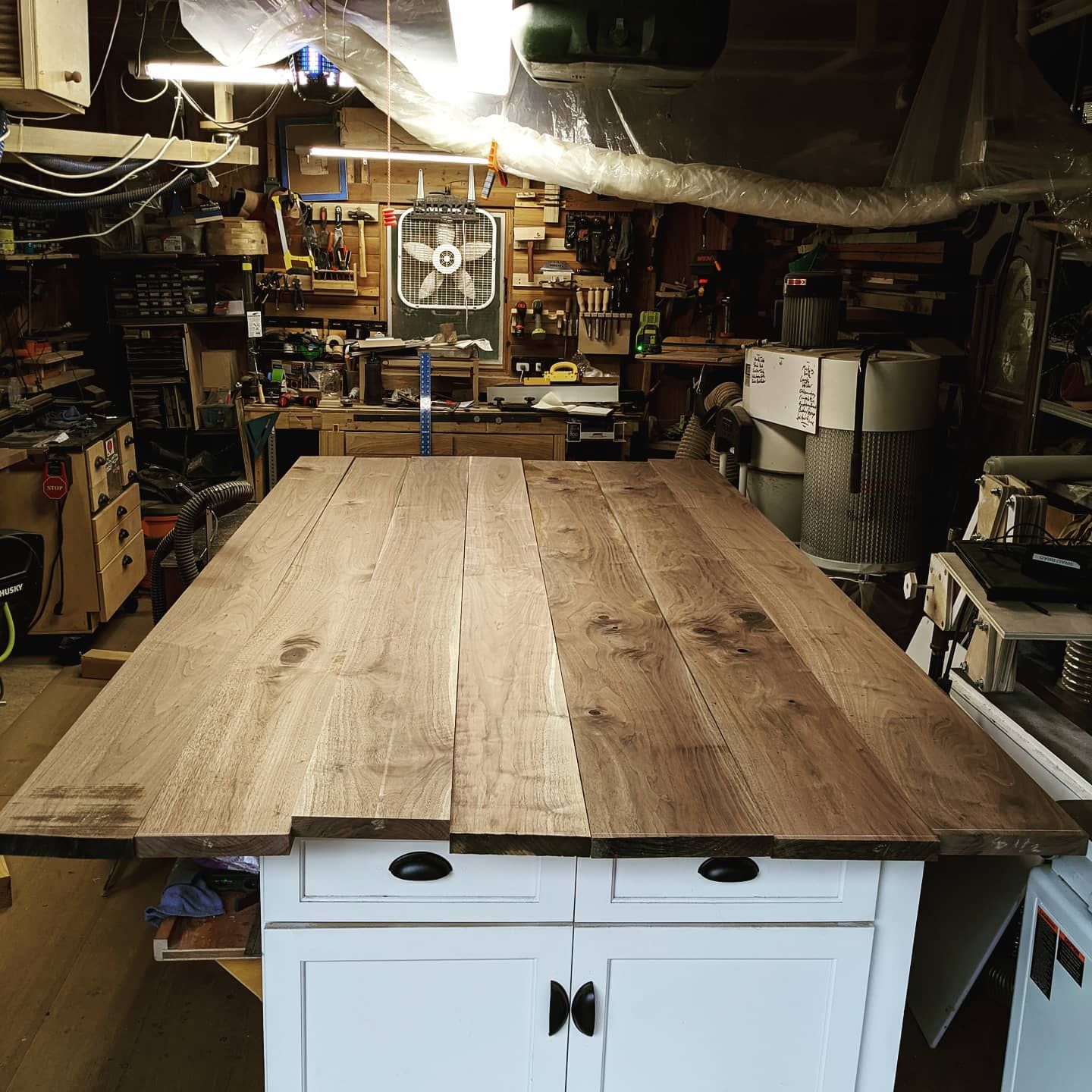 A large wooden table in a workshop with a fan hanging from the ceiling