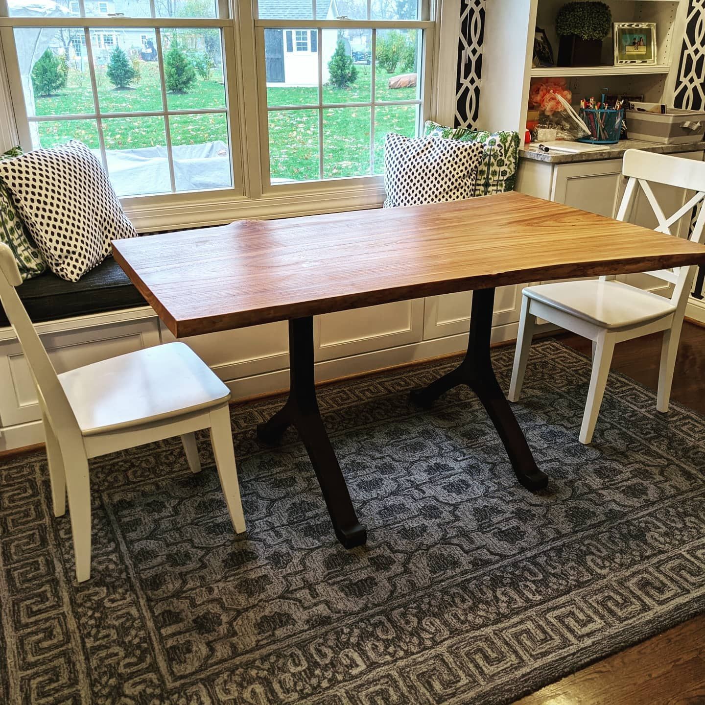 A wooden table and chairs are sitting on a rug in front of a window.