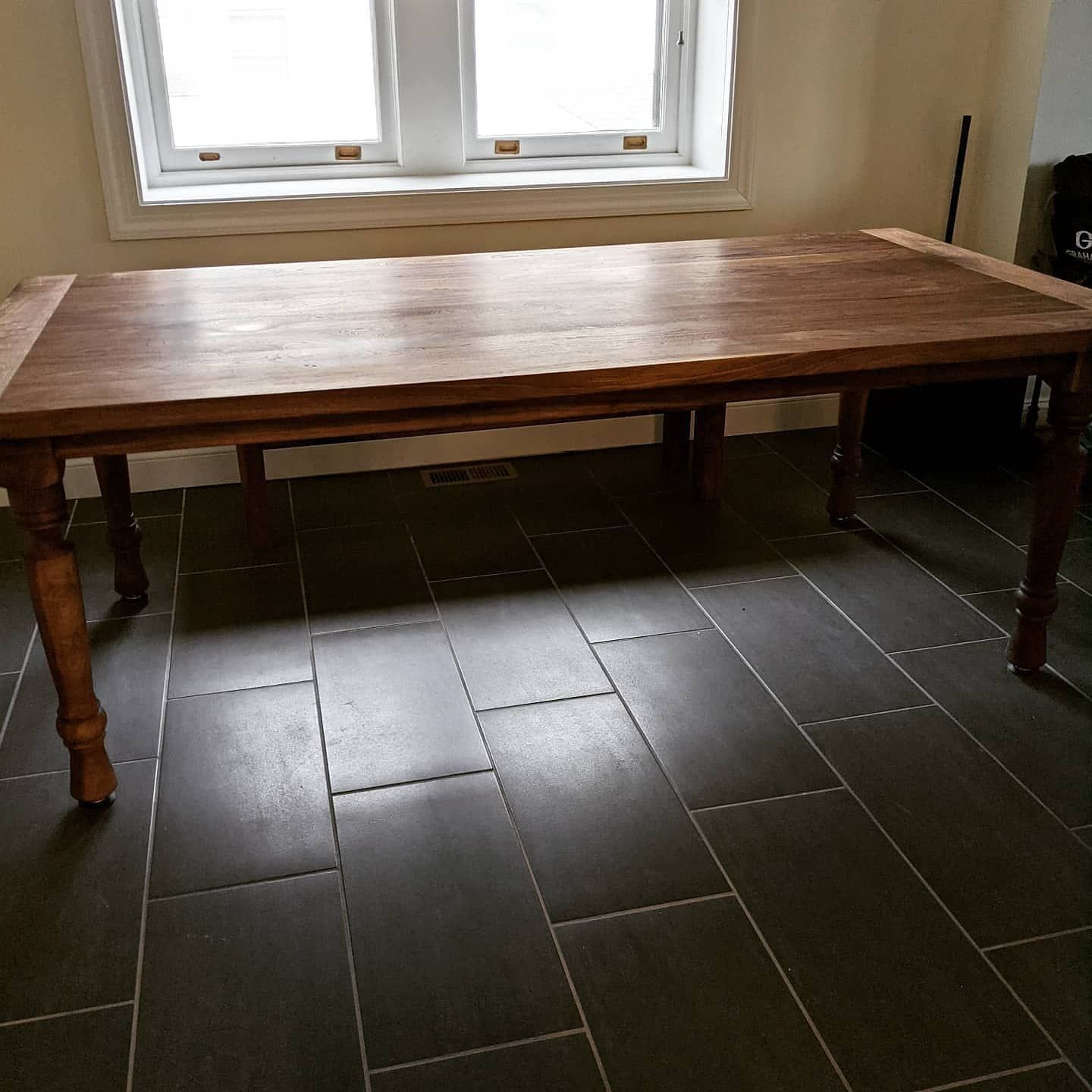 A wooden table is sitting on a tiled floor in front of a window.