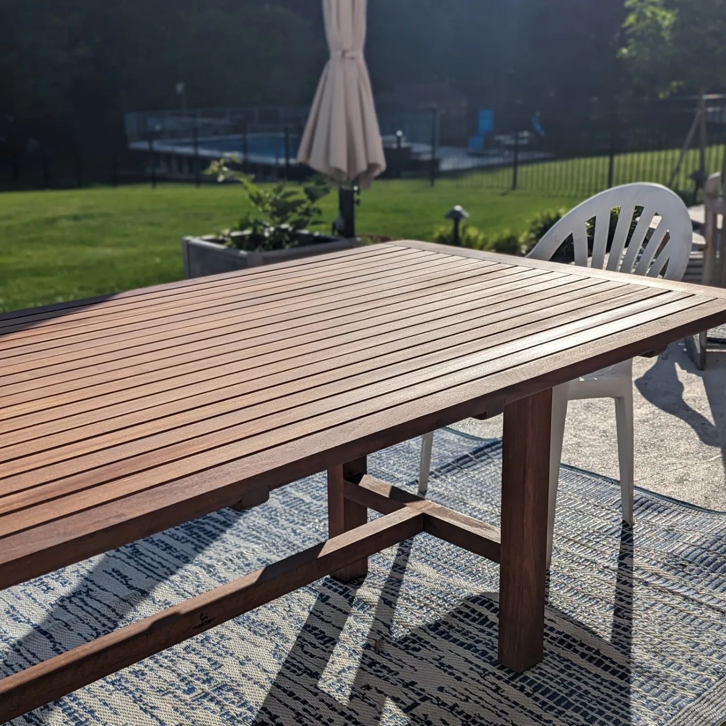 A wooden table and chairs on a patio with an umbrella in the background