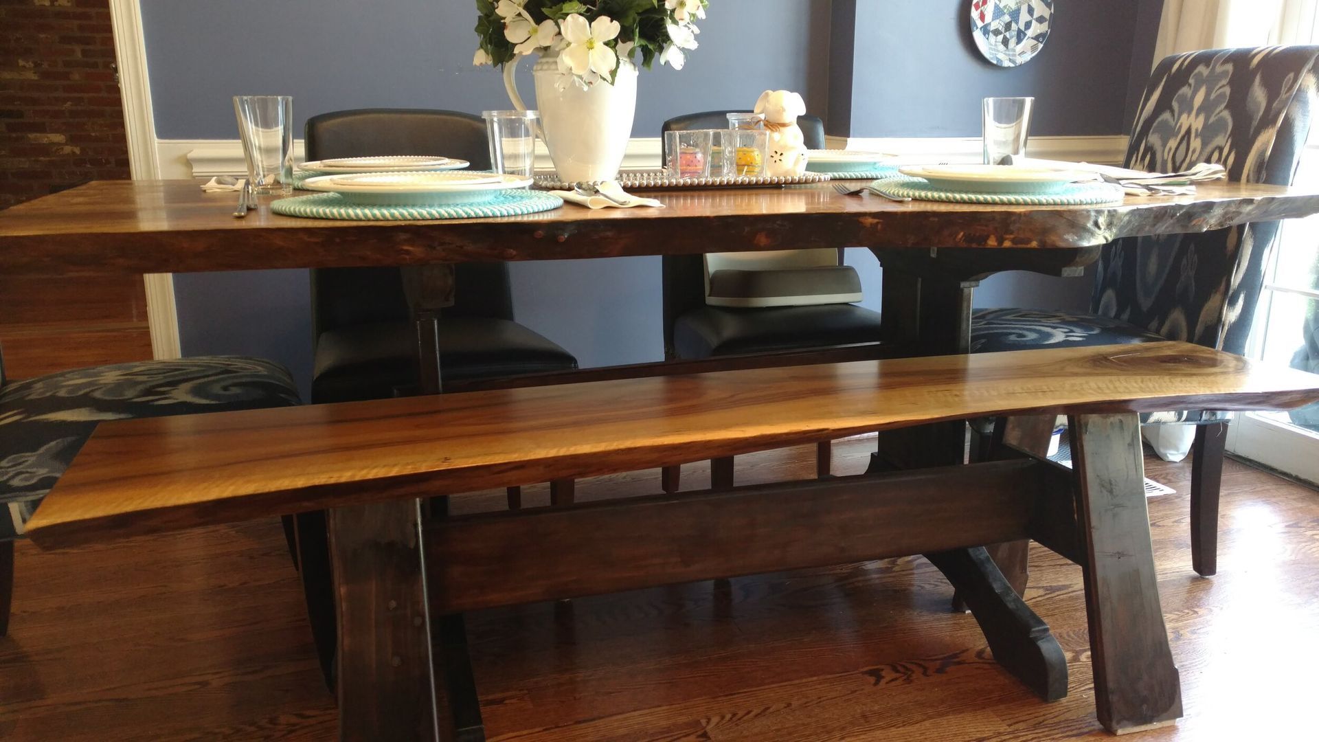 A dining room table with a bench and a vase of flowers on it.
