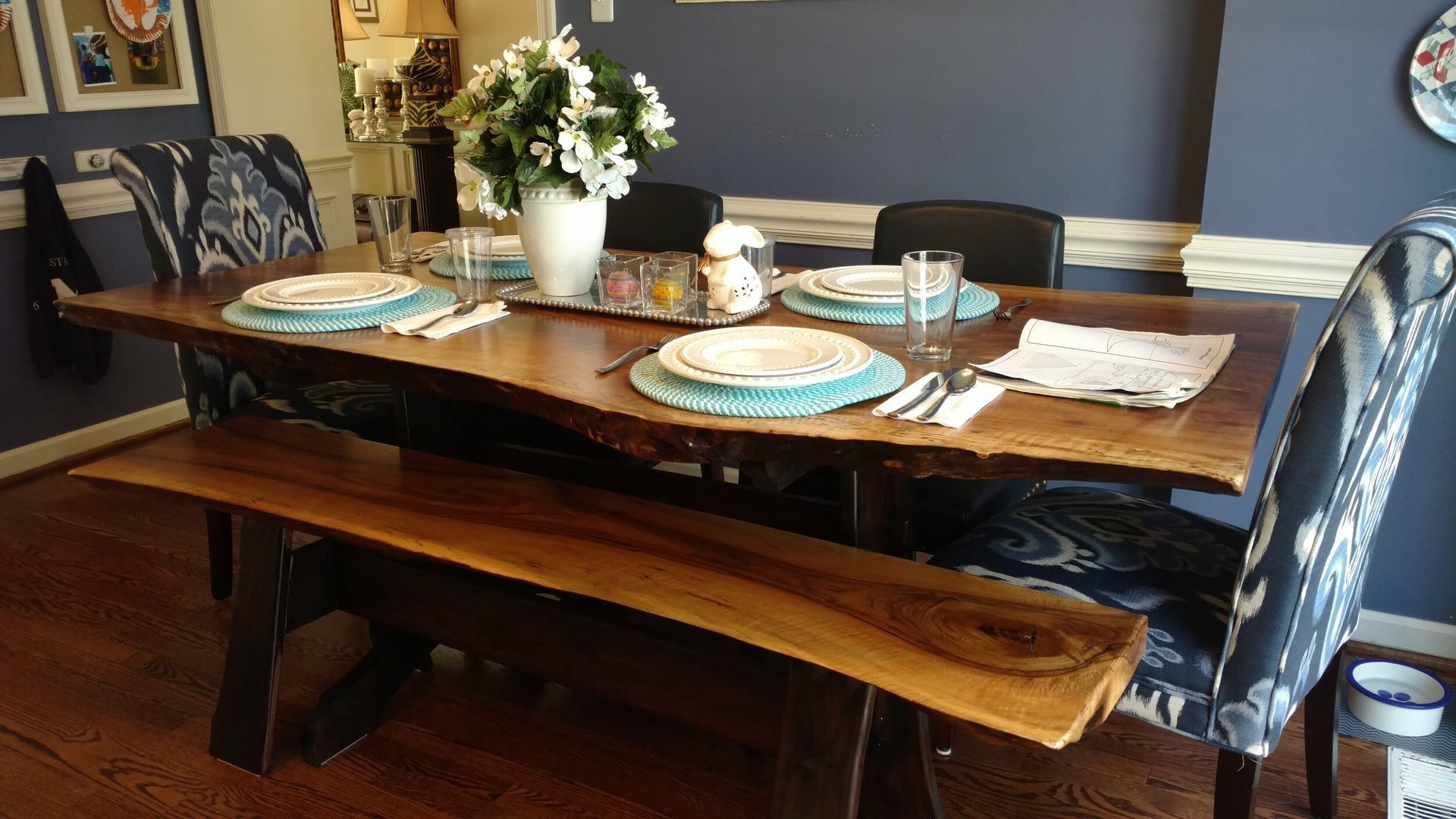 A dining room table with plates , glasses , and a bench.