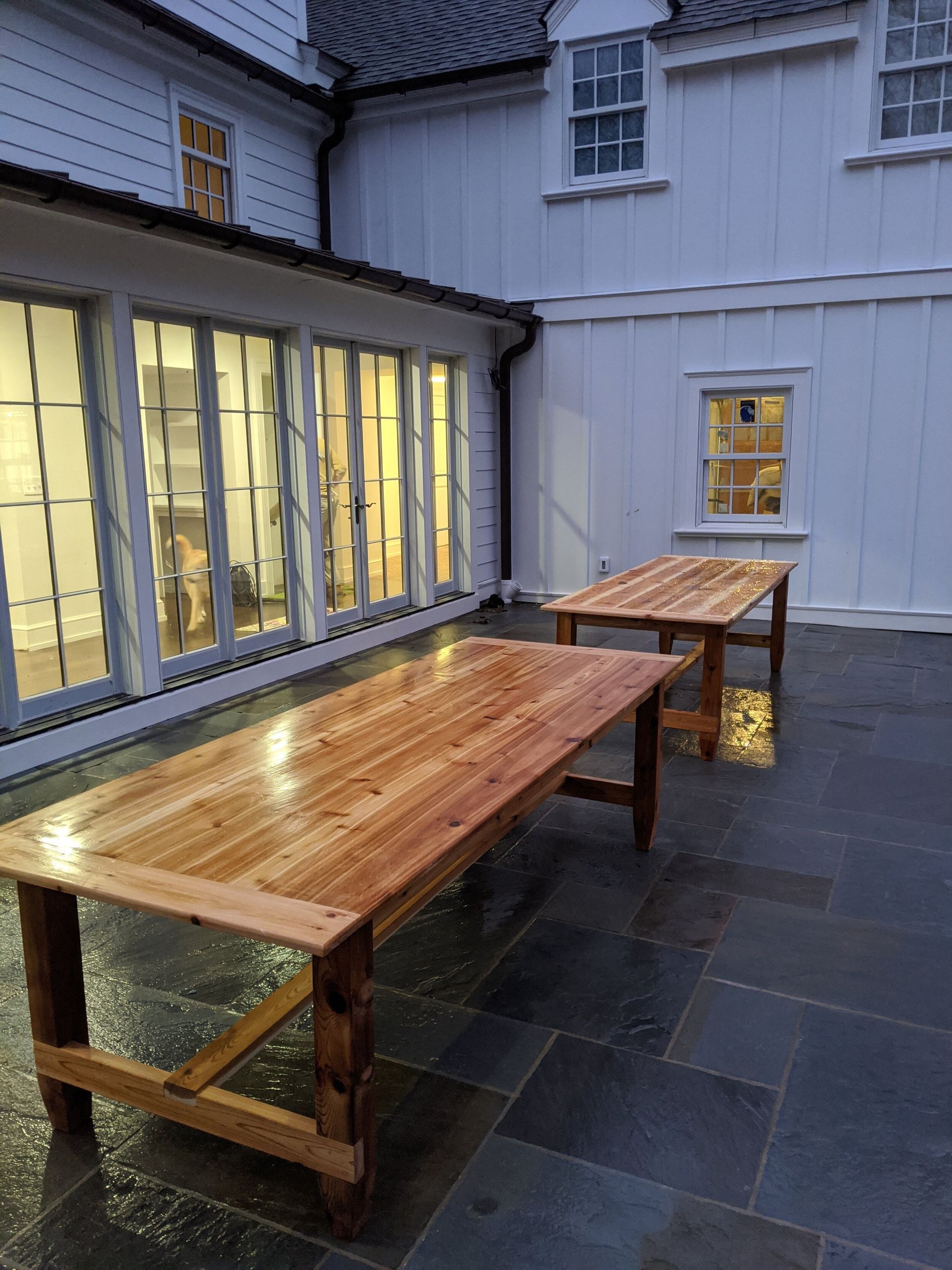 Two wooden tables are sitting on a patio in front of a white building.