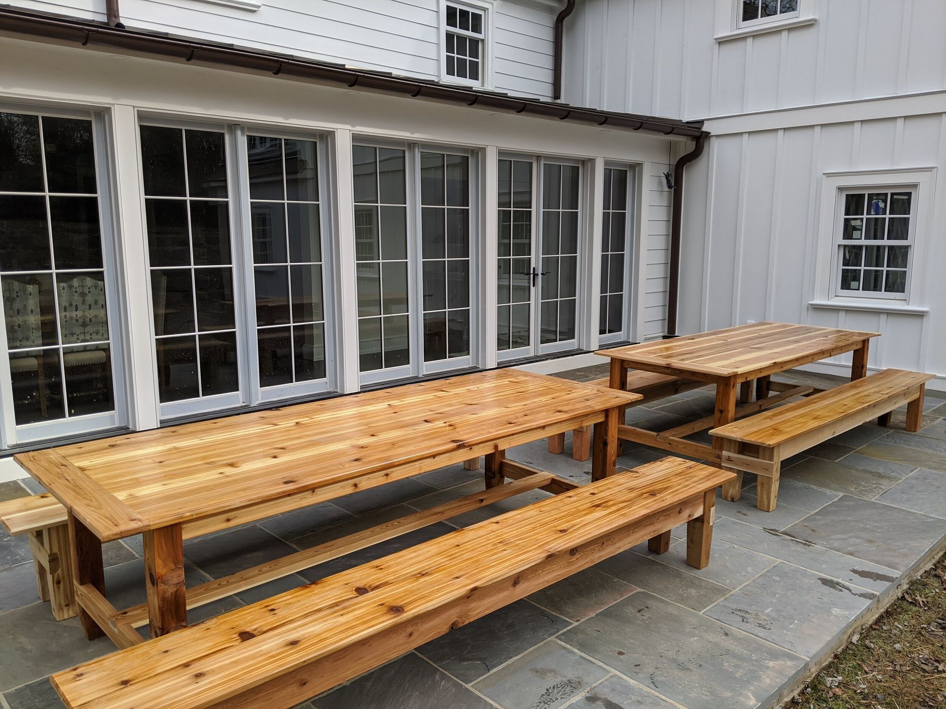 A large wooden picnic table with benches in front of a white house.