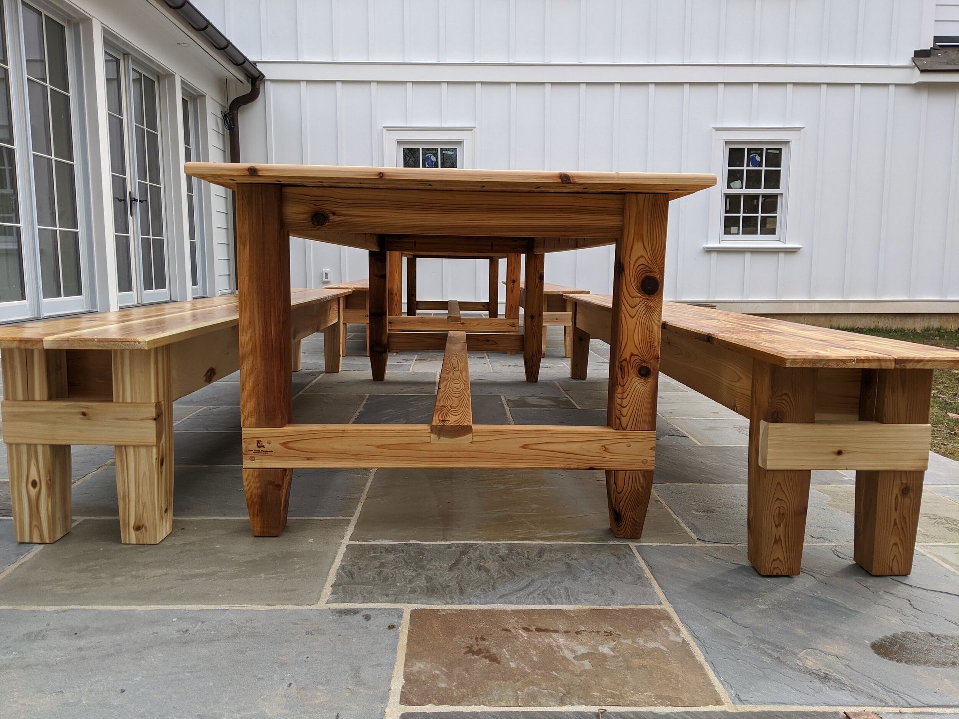 A wooden table and benches on a patio in front of a white house