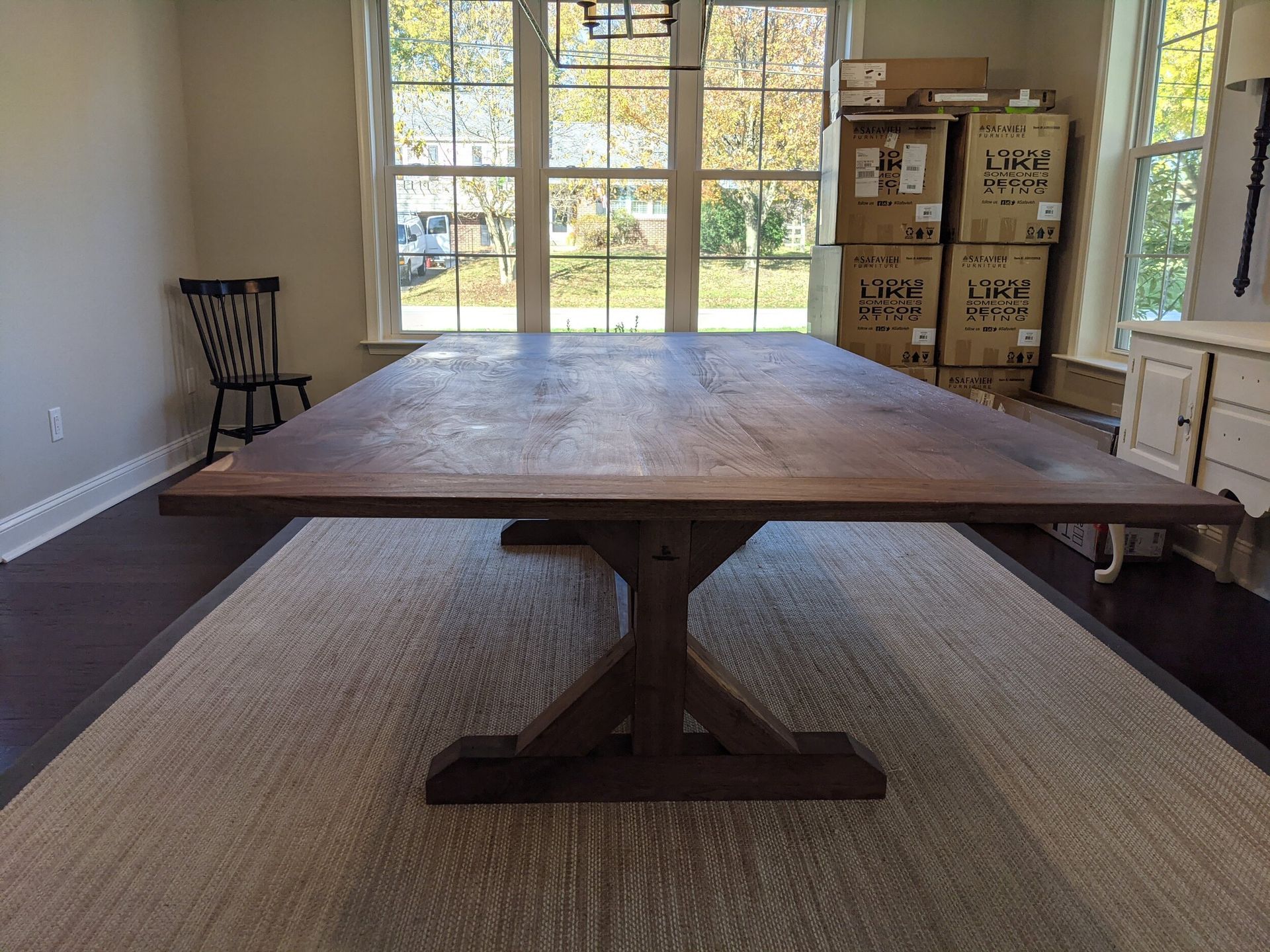 A large wooden table is sitting in a living room next to a window.