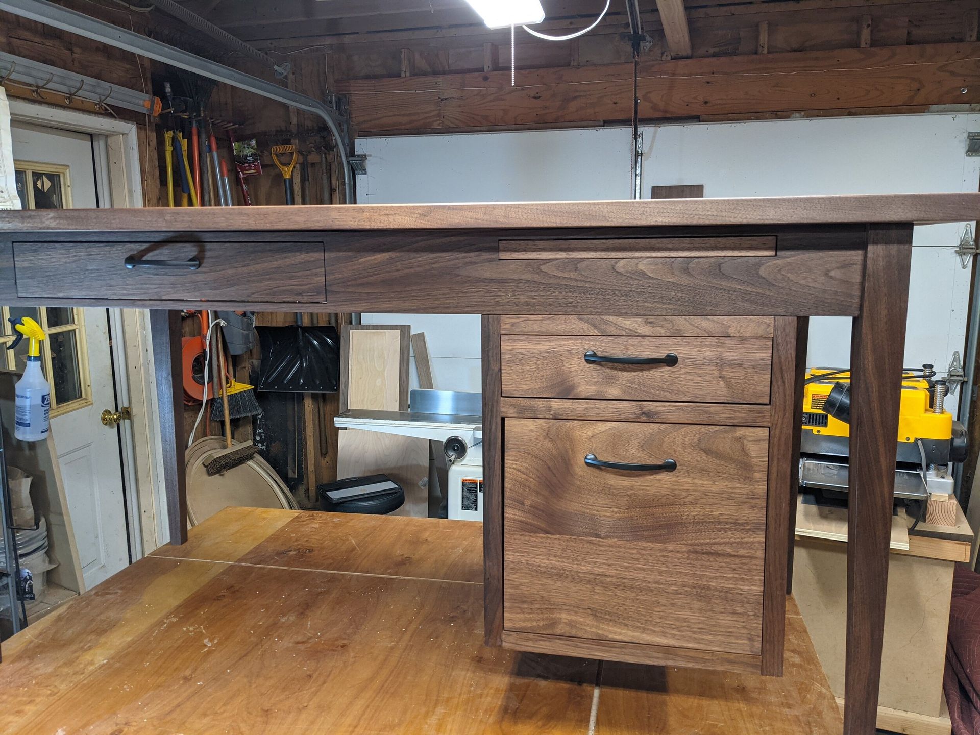 A wooden desk with drawers is sitting on top of a wooden table in a garage.