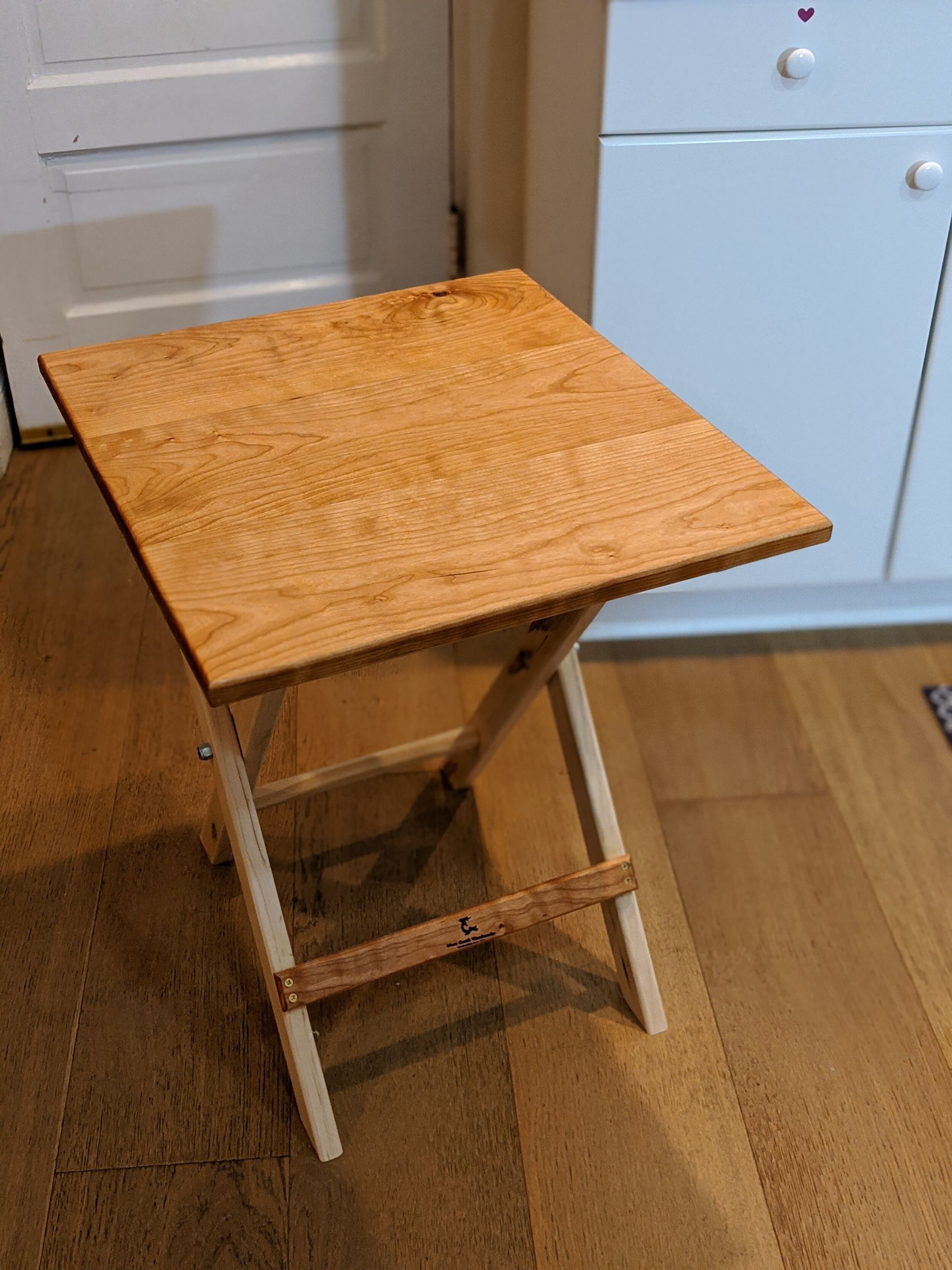 A small wooden folding table is sitting on a wooden floor.