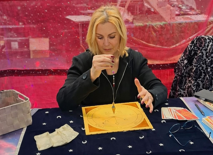 Una persona tiene un pendolo sopra un grafico circolare steso su una tovaglia blu con motivi di stelle e lune.