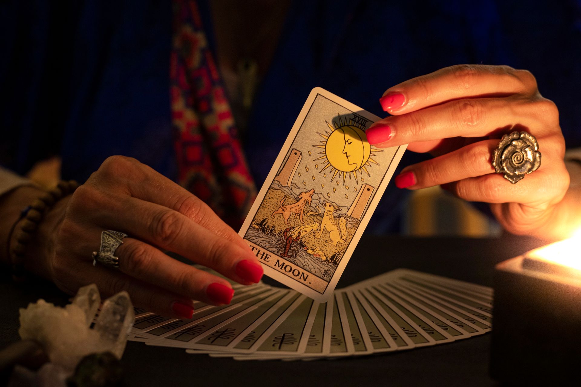 In uno spazio scarsamente illuminato da candele, una persona con le unghie dipinte tiene in mano la carta dei tarocchi 