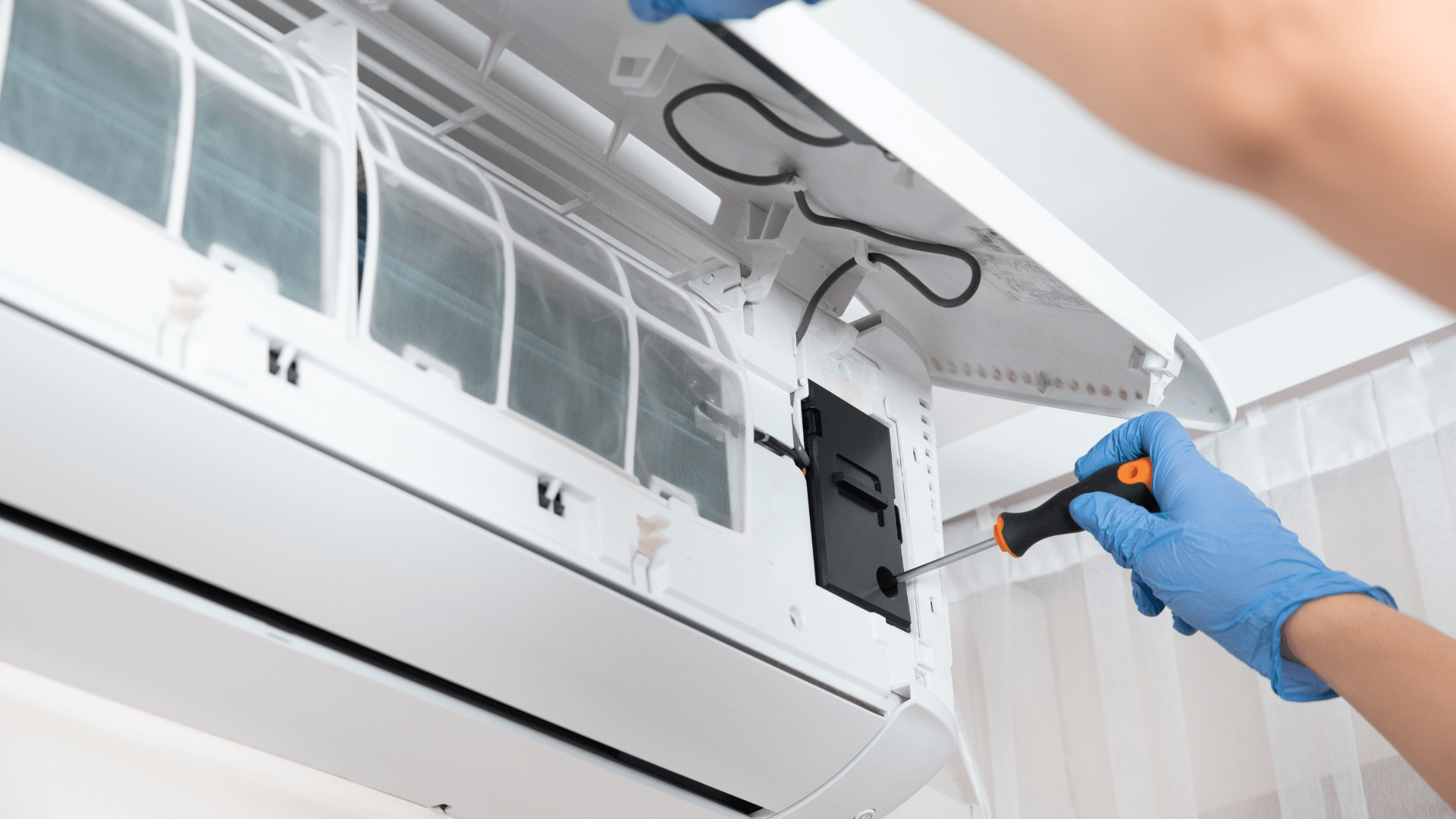 A person is fixing an air conditioner with a screwdriver.