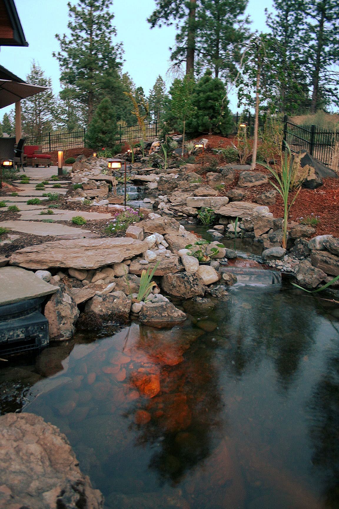 A landscaped pond with cascading water features and stepping stones, surrounded by rocks and greenery.