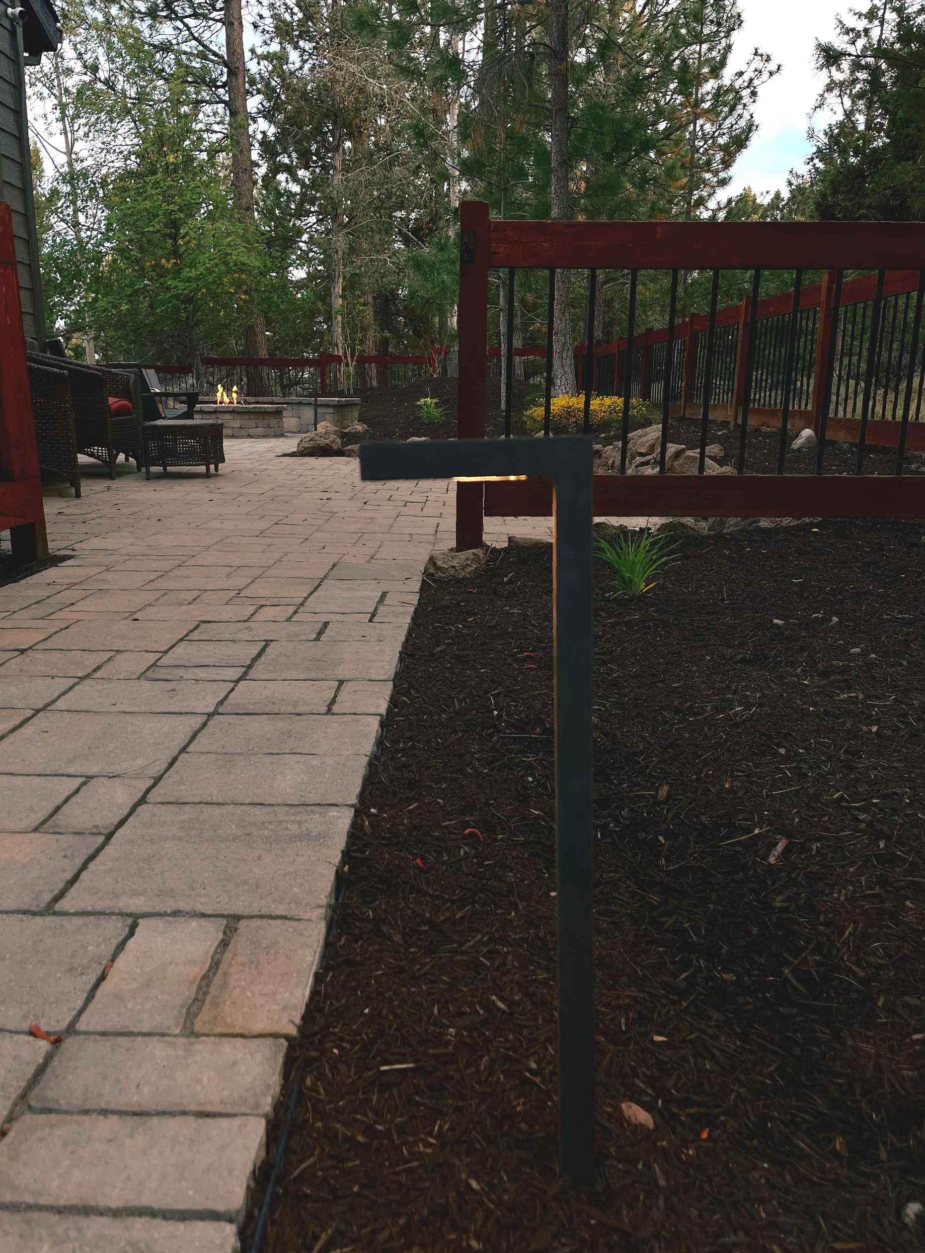 A pathway made of stone pavers alongside a dark mulch bed, a black metal post light, and a red fenced deck.