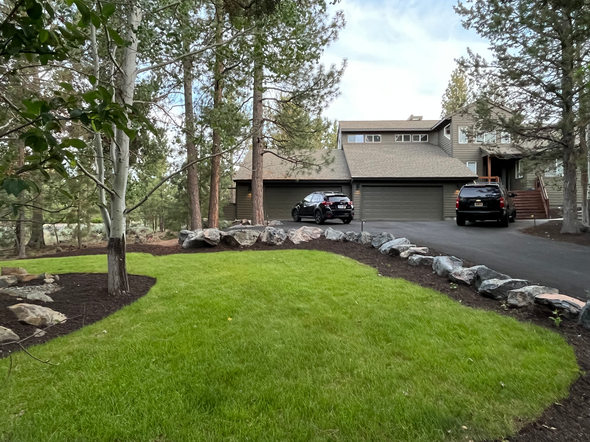 A house with a driveway, green lawn, and rock landscaping. Two cars are parked in front of the garage.
