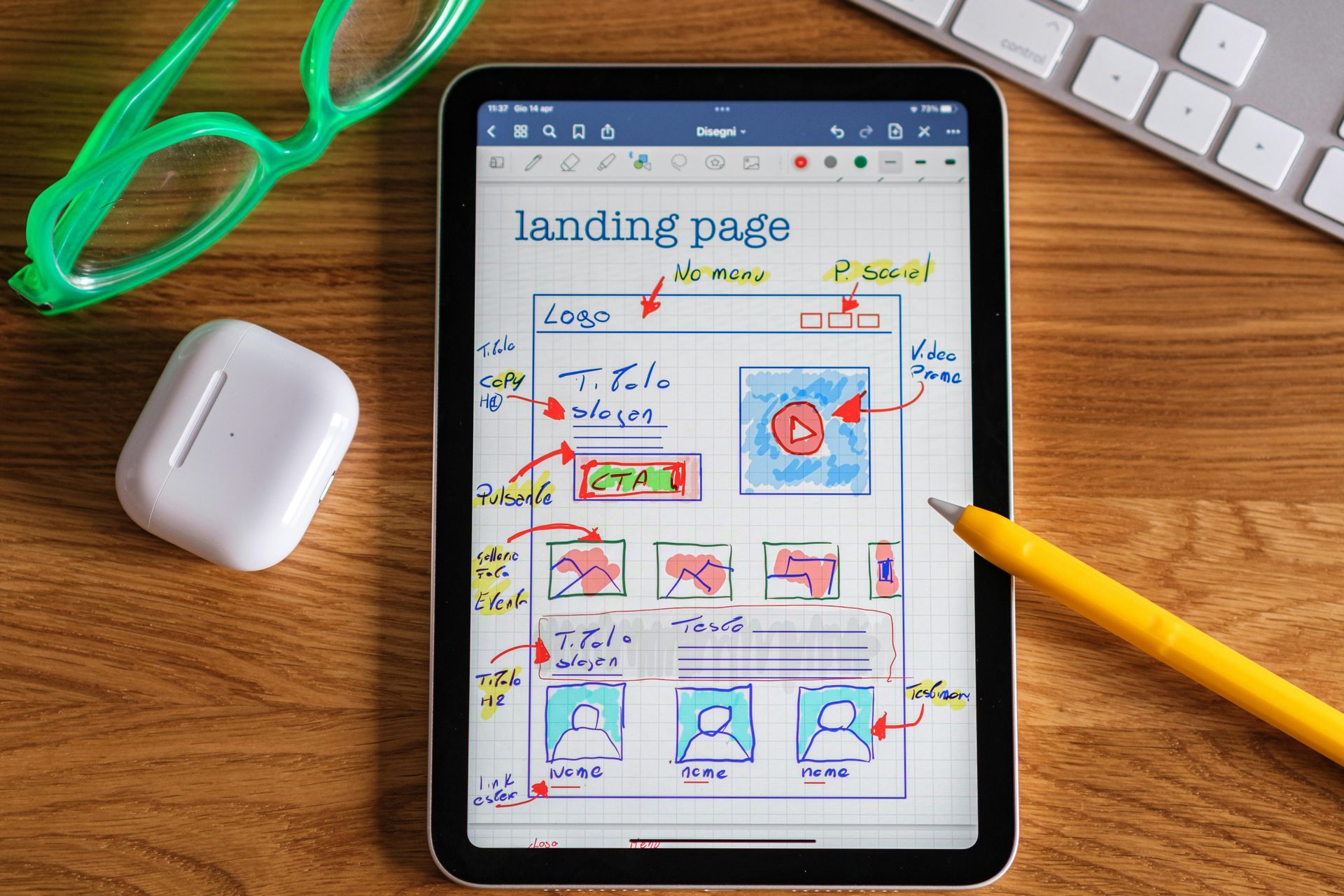 A sketch of layout of a landing page on a tablet device with a pen and glasses on a wooden table.