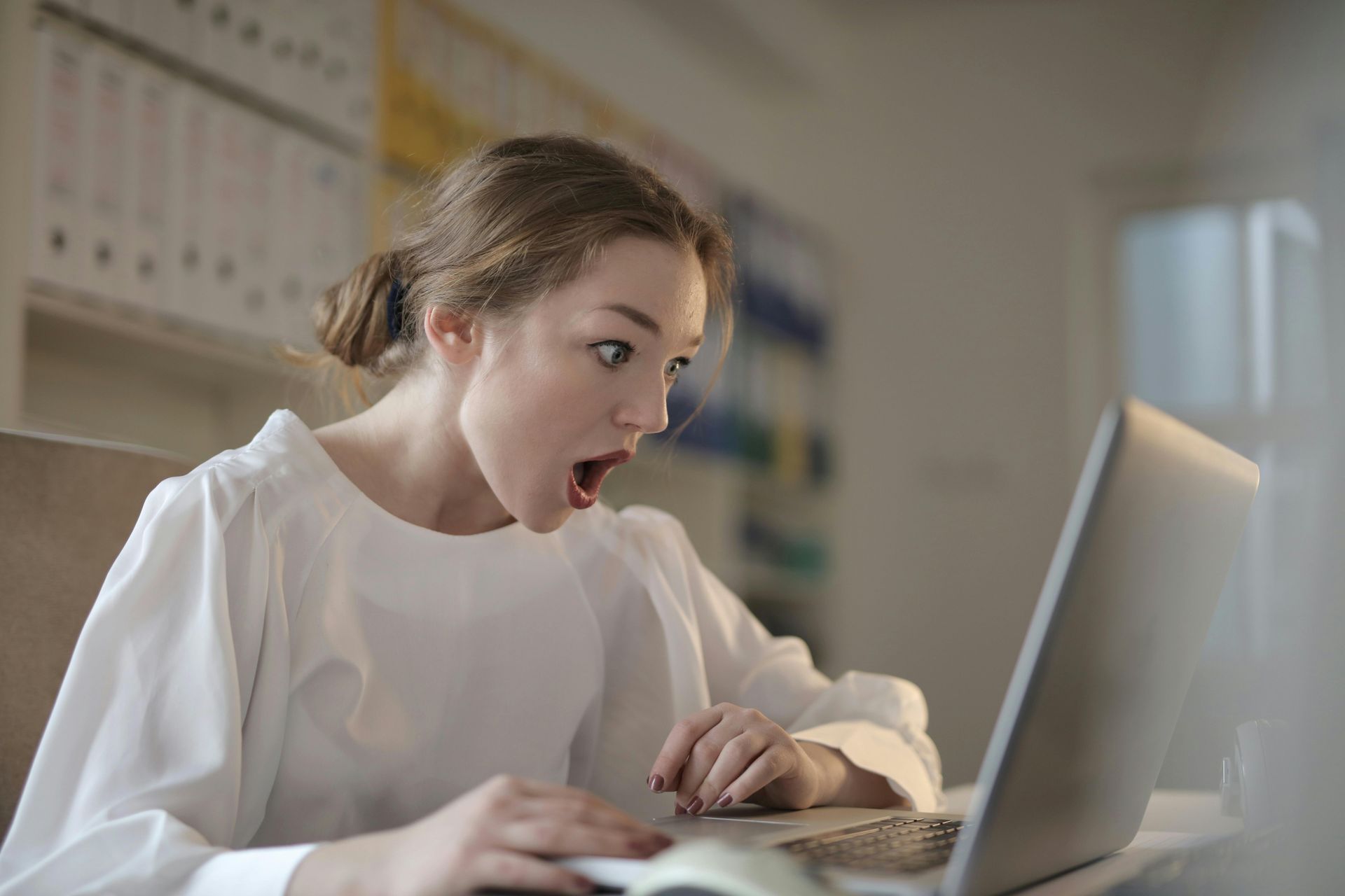 A woman is sitting at a desk using a laptop computer with a surprised look with the cost of building a website