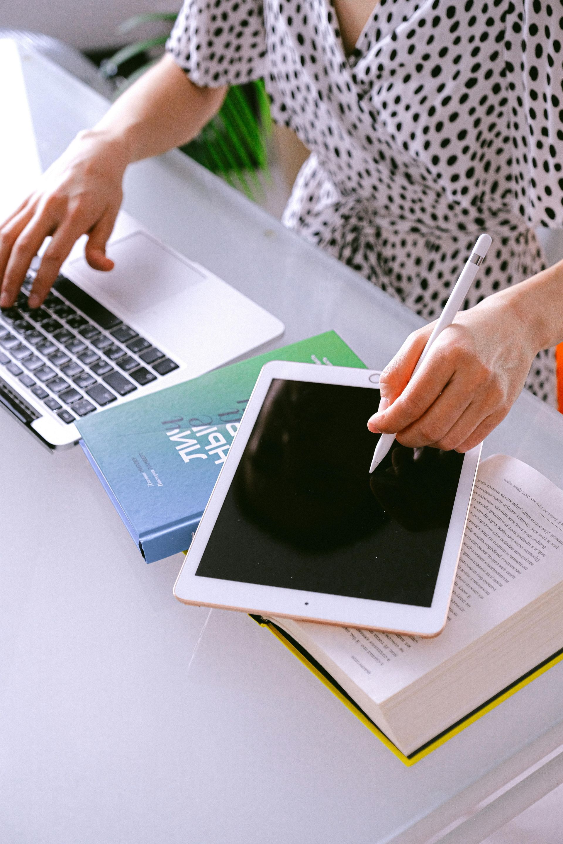 A woman is sitting at a desk using a laptop and a tablet.