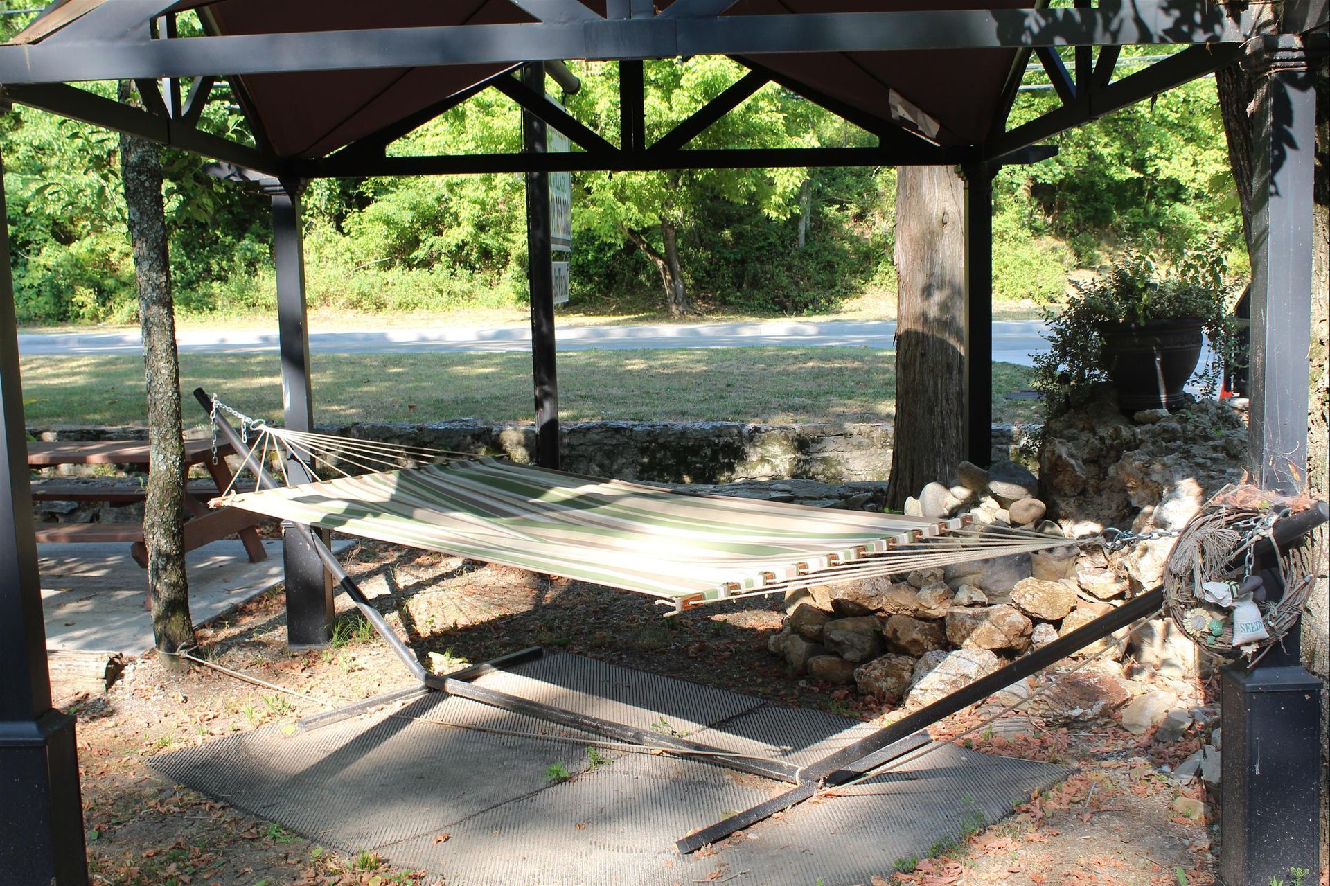 A hammock is sitting under a gazebo in the woods