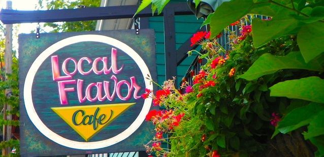 A sign for local flavor cafe is surrounded by flowers.