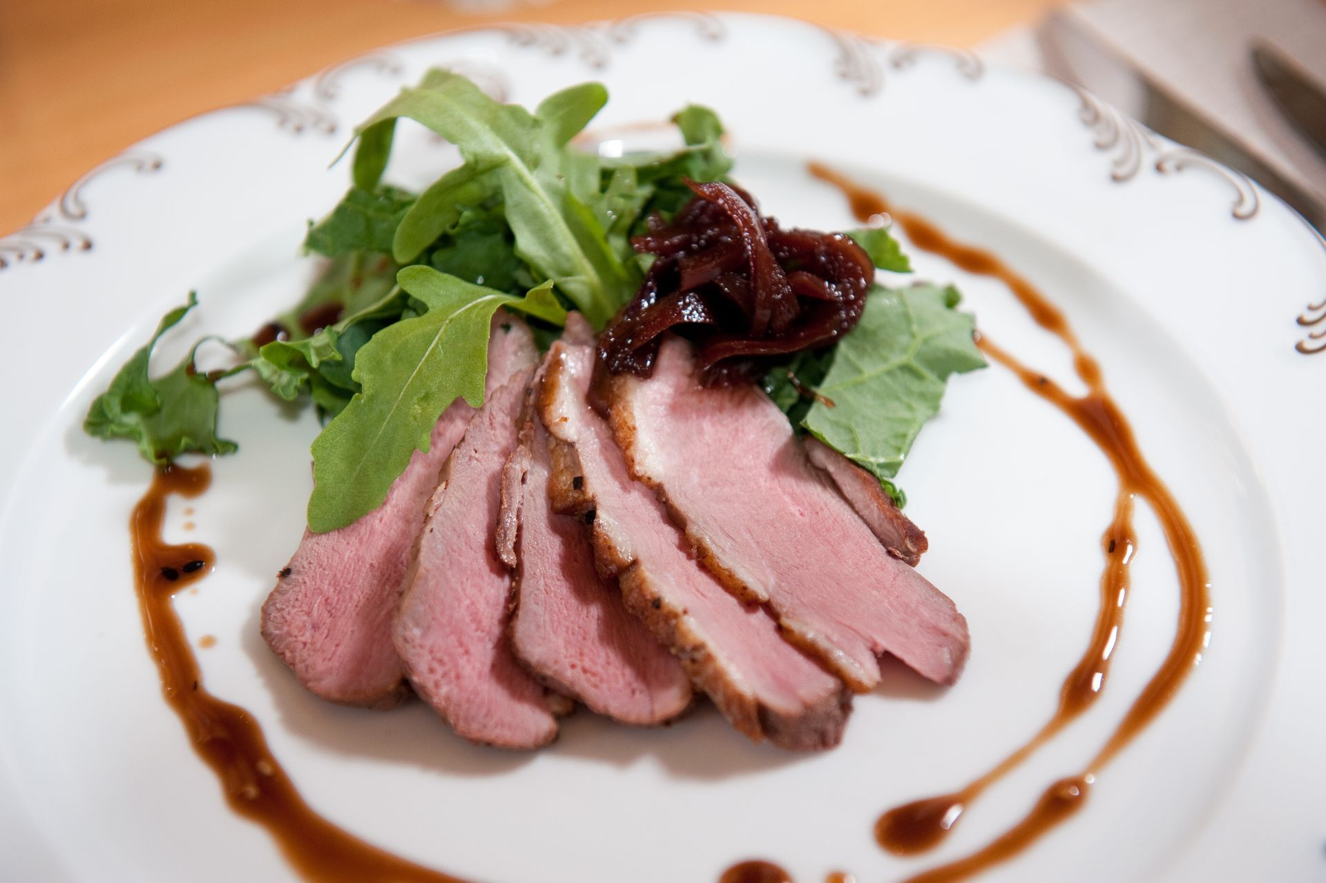 A white plate topped with sliced meat and greens
