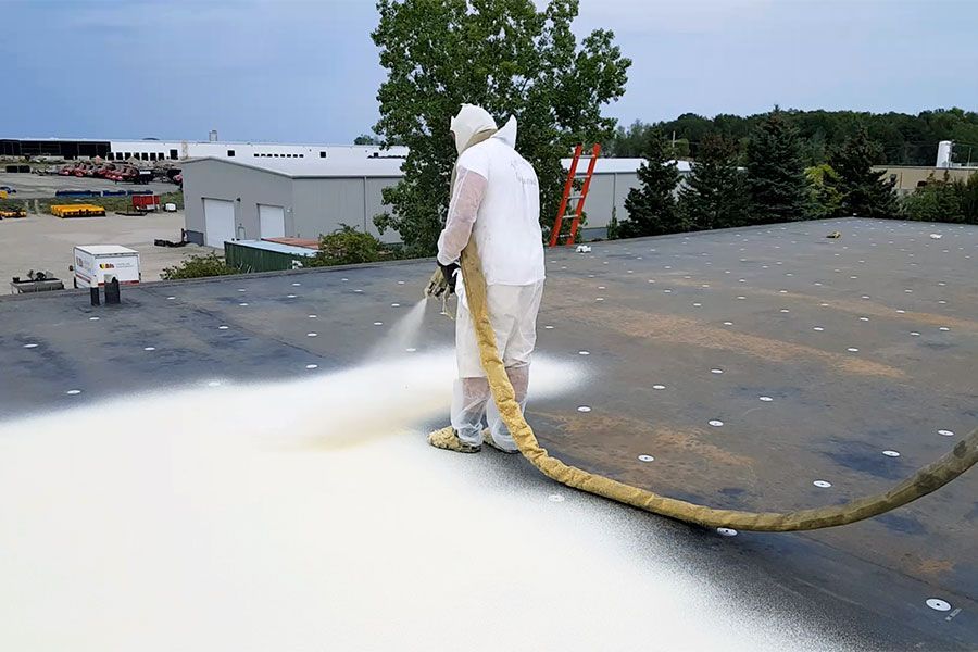 Person in protective suit sprays white coating on flat roof.