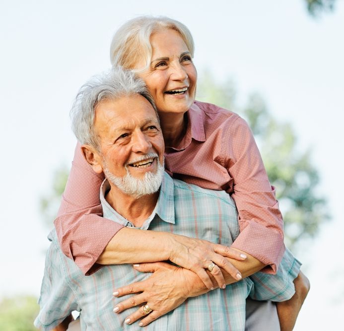 A woman is giving an older man a piggyback ride.