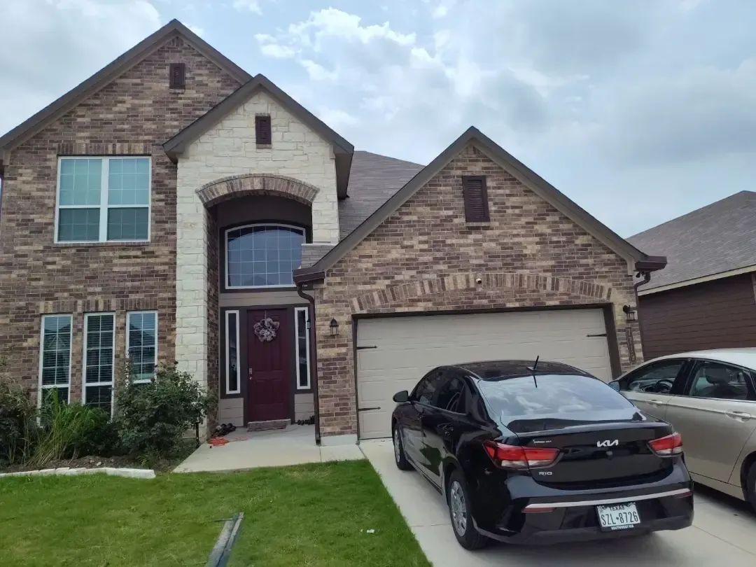 A black car is parked in front of a large brick house.