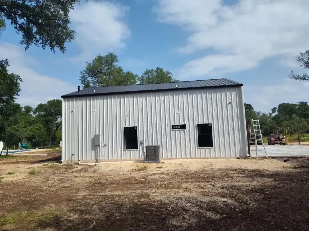 A white building with a black roof is sitting in the middle of a dirt field.