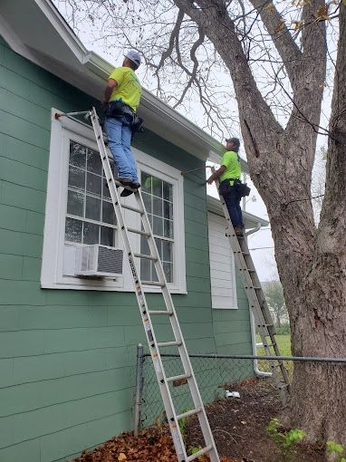 AquaWorks Rain Gutters - Two workers on ladders cleaning gutters of a green house; one worker near a tree.