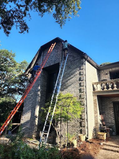 AquaWorks Rain Gutters - Two people on ladders working on the roof of a brick house. Blue sky and trees surround the building.