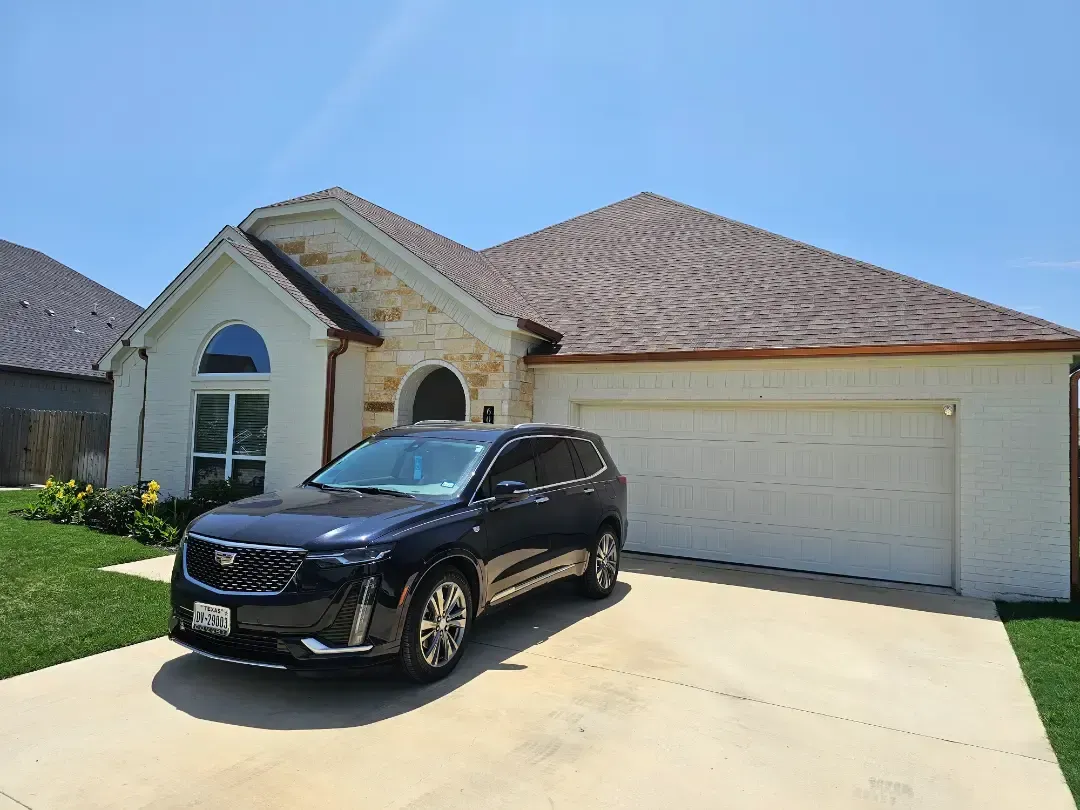 A black car is parked in front of a white house.