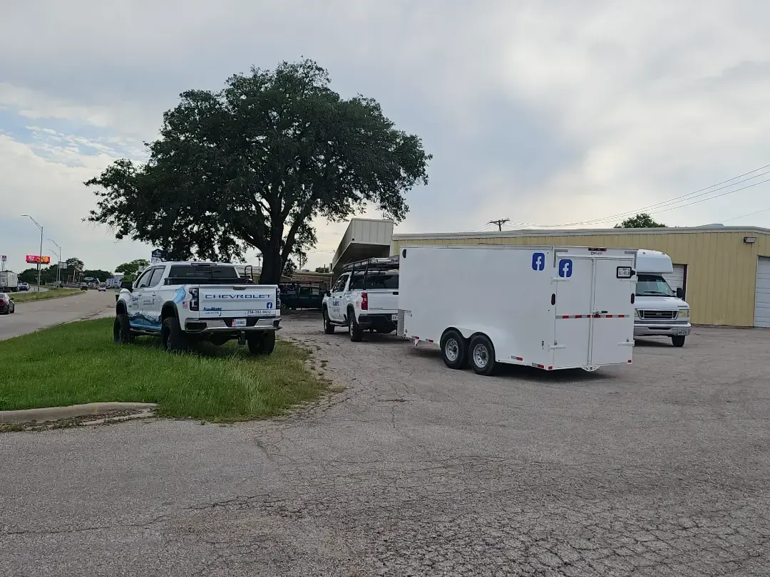A truck and trailer are parked in a gravel lot in front of a building.