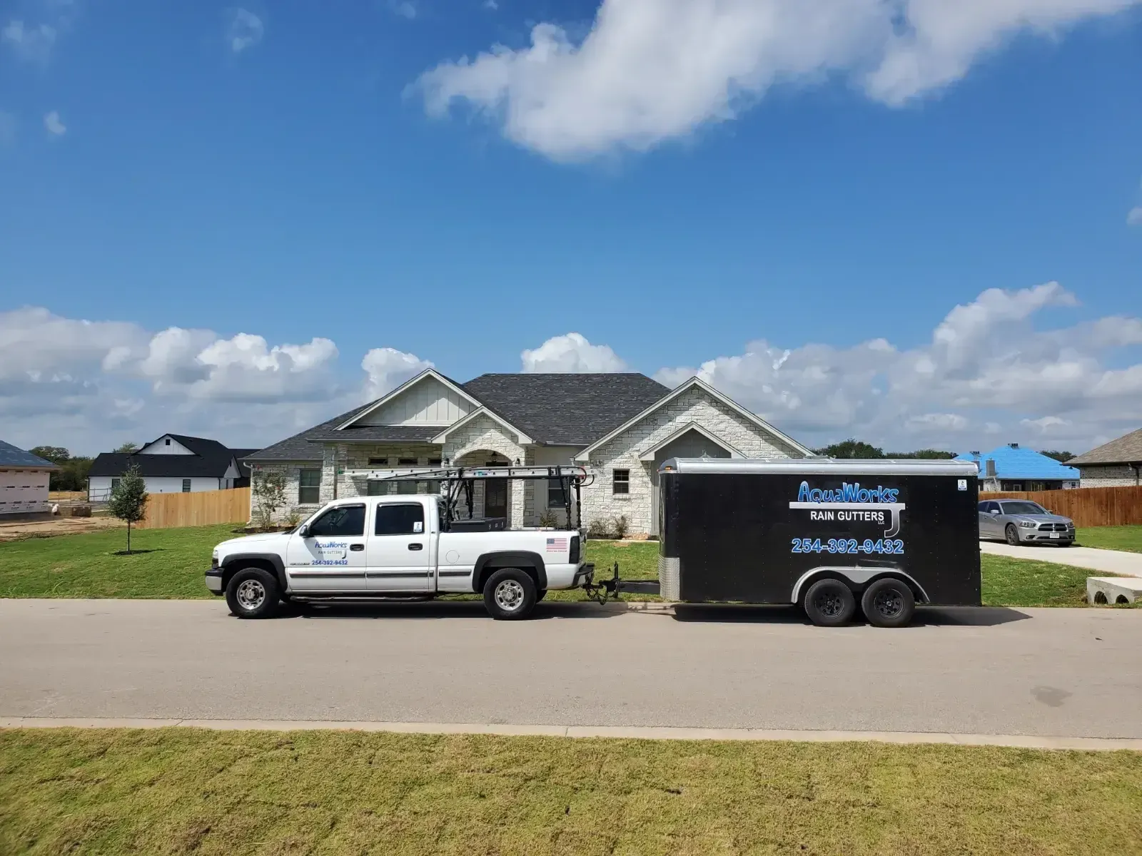 A white truck with a trailer attached to it is parked in front of a house.