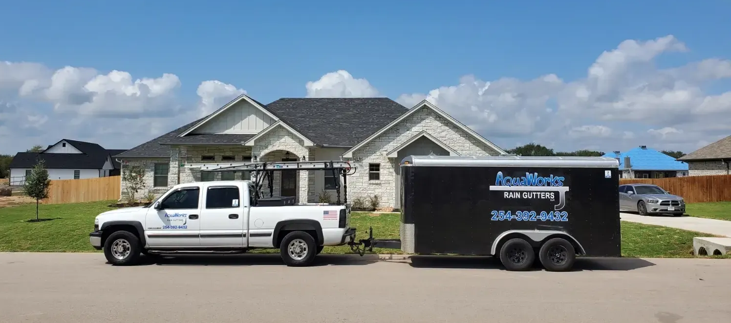 AquaWorks Rain Gutters - White truck with trailer in front of a house on a sunny day. The trailer has a business logo.