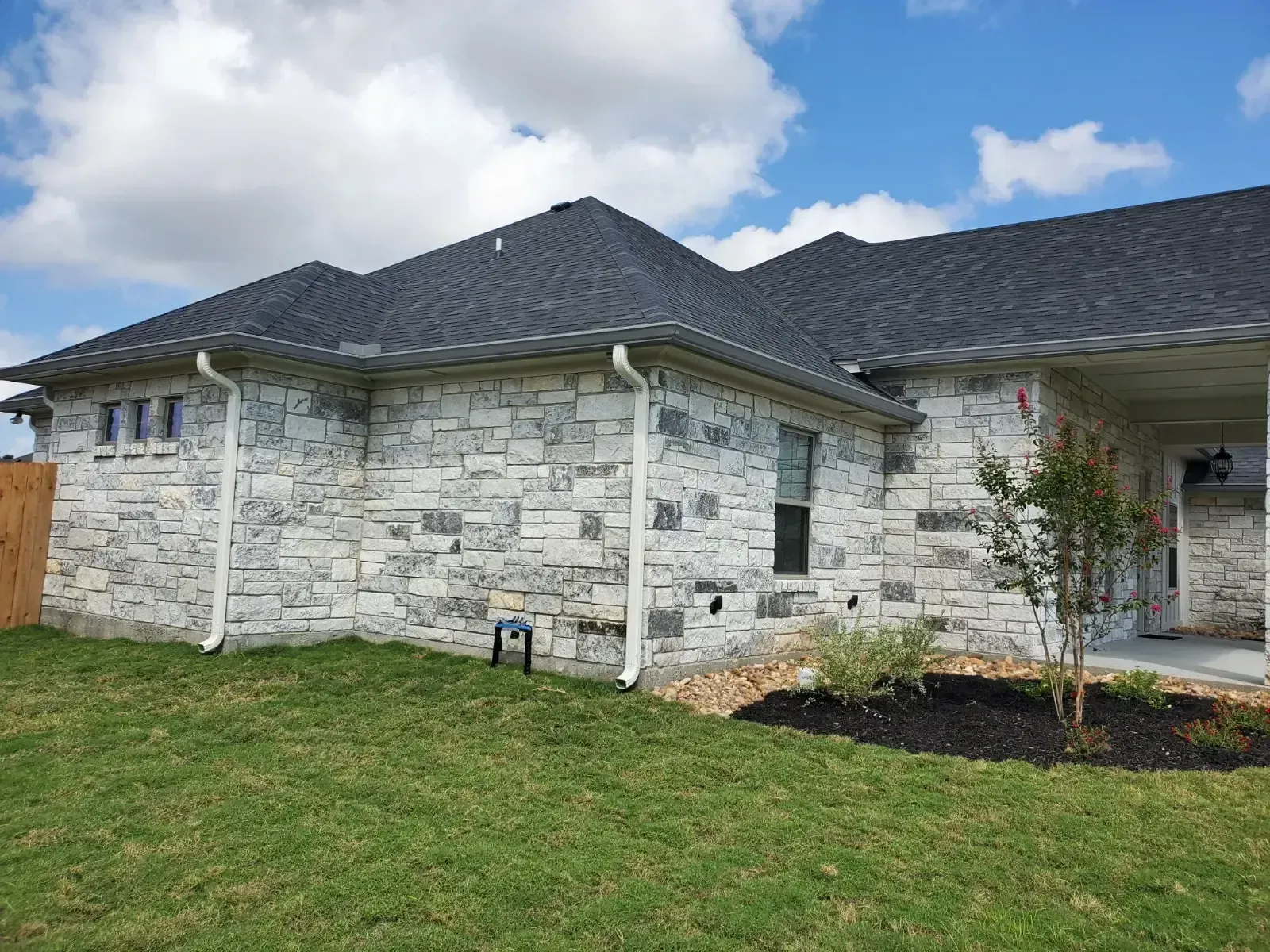 A white brick house with a black roof is sitting on top of a lush green lawn.
