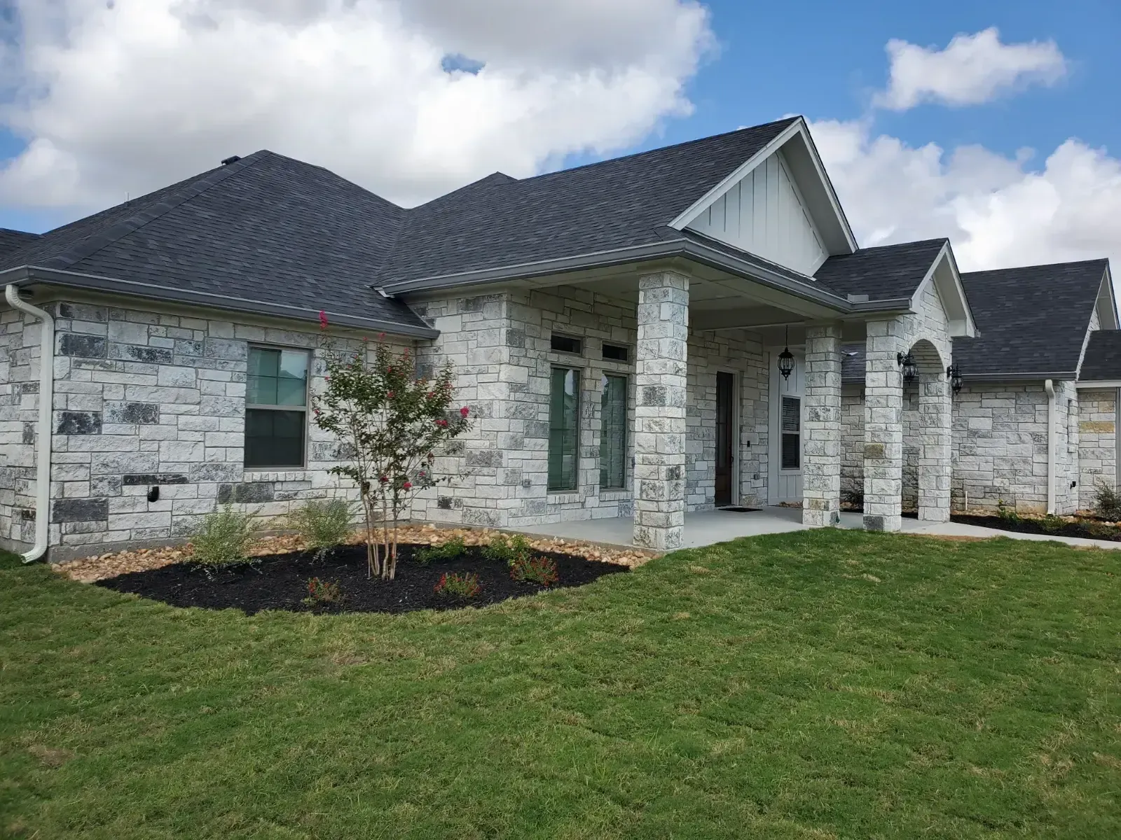 A large white brick house with a black roof and a large lawn in front of it.