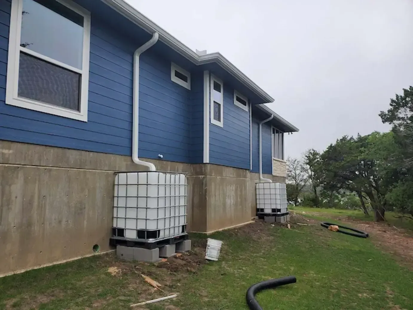 A blue house with white trim and gutters is sitting on top of a lush green field.