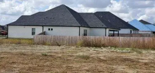A white house with a black roof is sitting in the middle of a field.