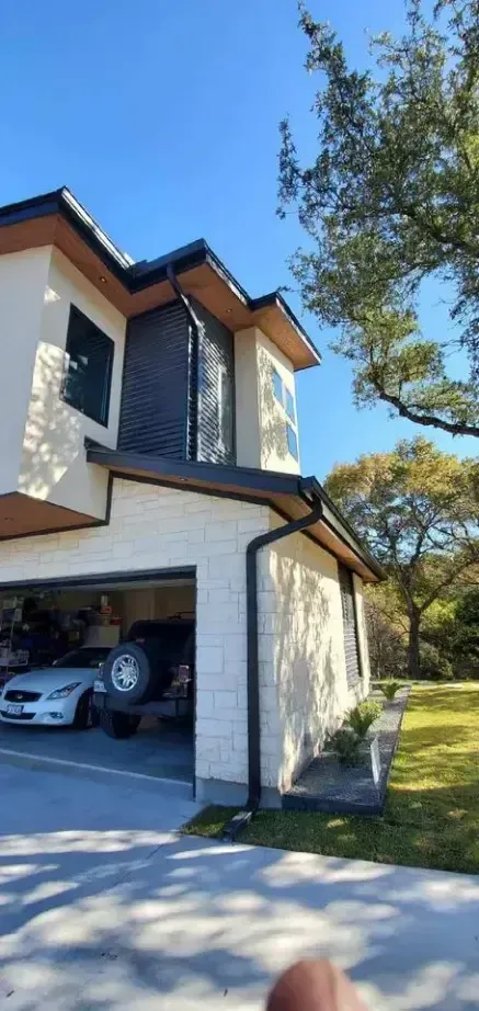 A person is standing in front of a house with a car parked in the garage.
