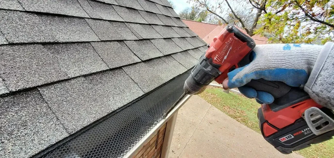 A person is using a drill to fix a gutter on a roof.