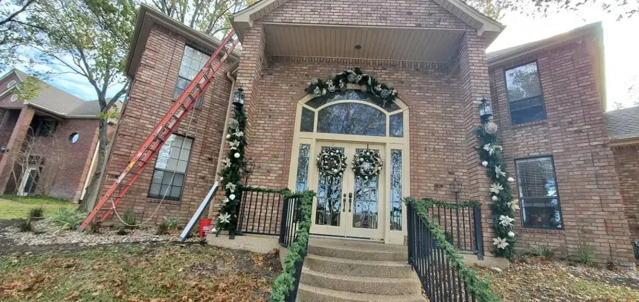 A large brick house with a ladder in front of it is decorated for christmas.