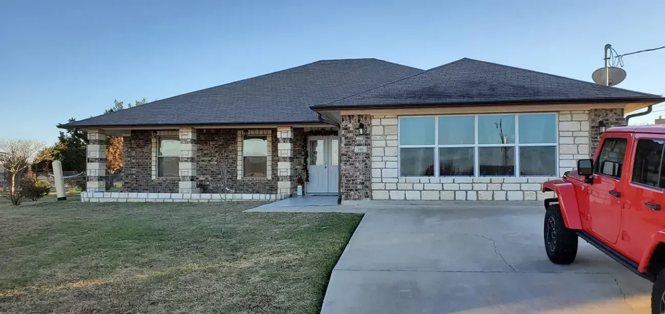A red jeep is parked in front of a brick house.