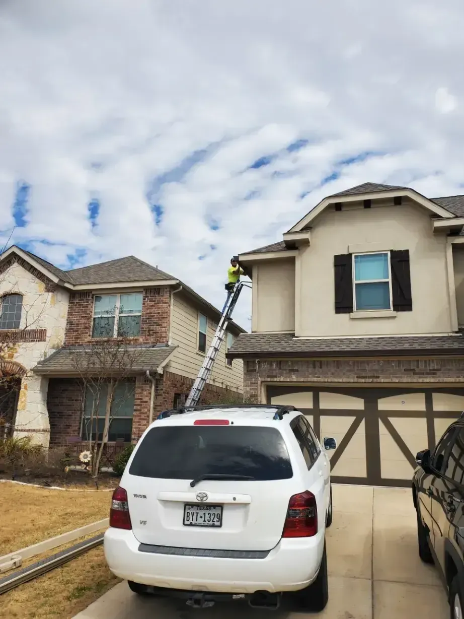 A white suv is parked in front of a house with a ladder attached to it.