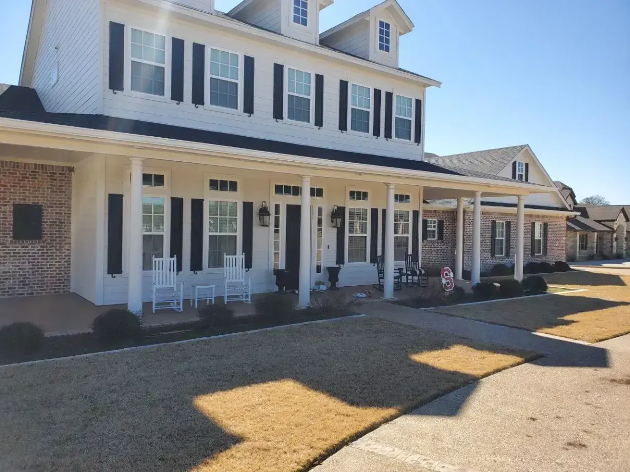 A large white house with a porch and chairs in front of it.